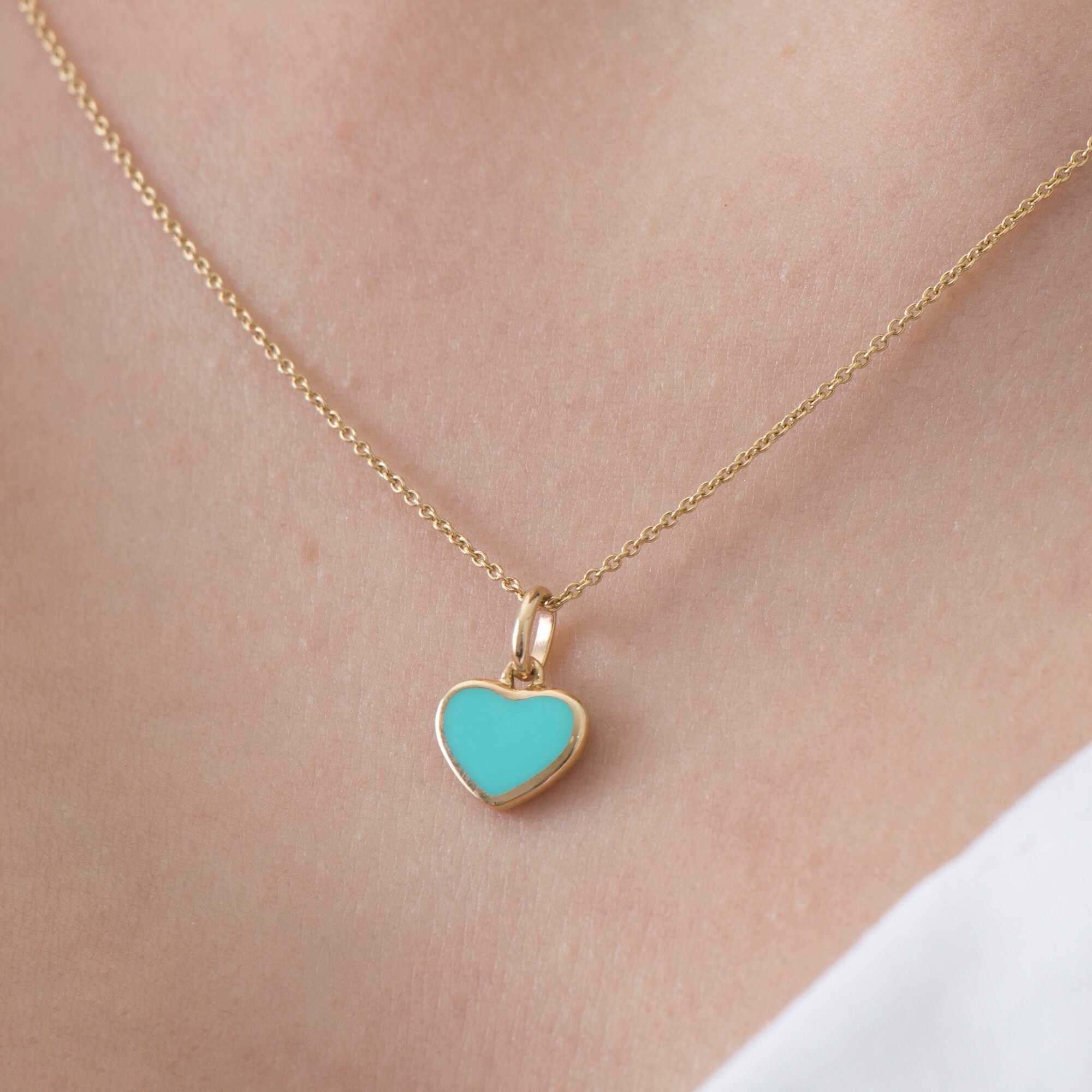 A model wearing a 14k yellow gold turquoise heart pendant on a thin gold chain.