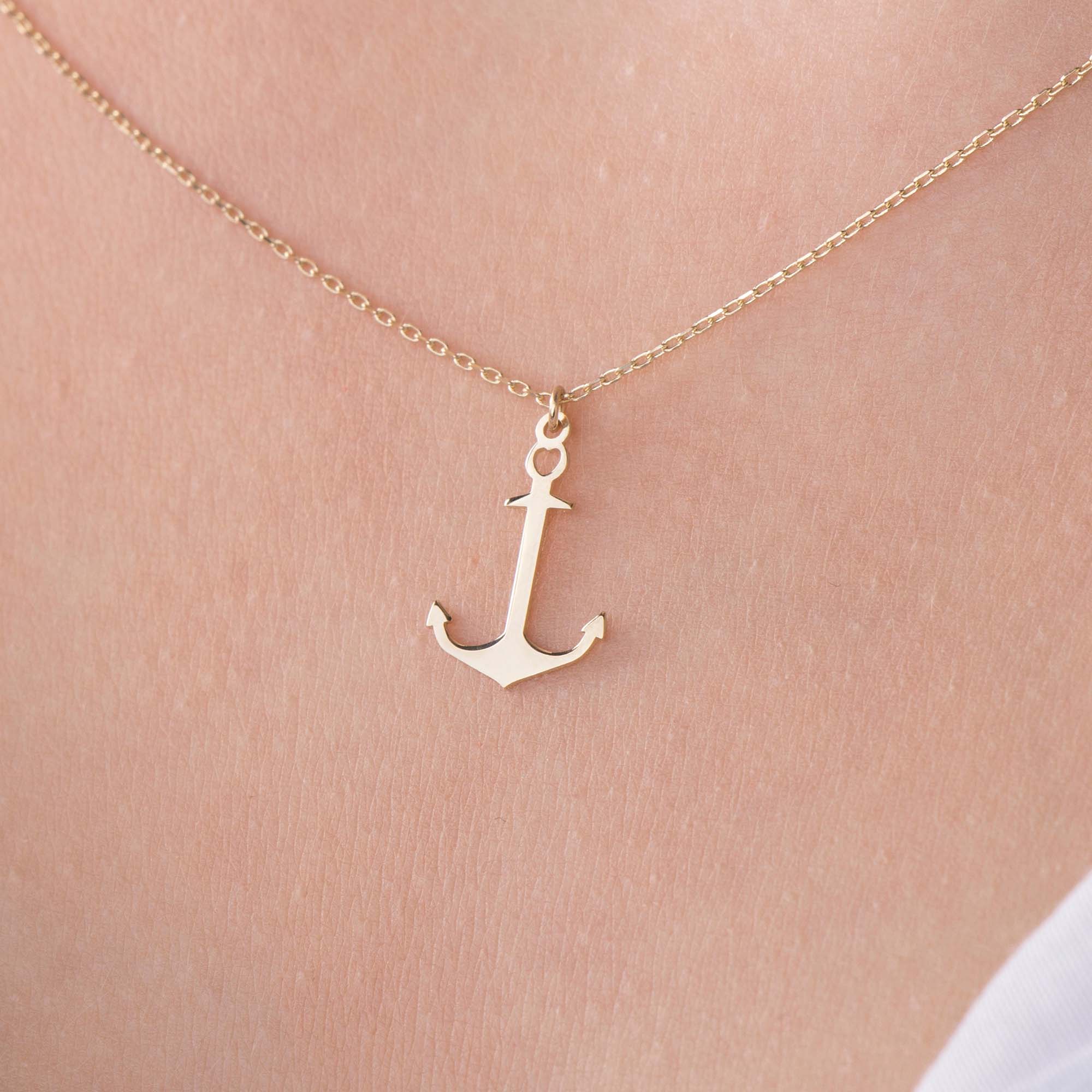 A minimal gold anchor necklace on a person's neck