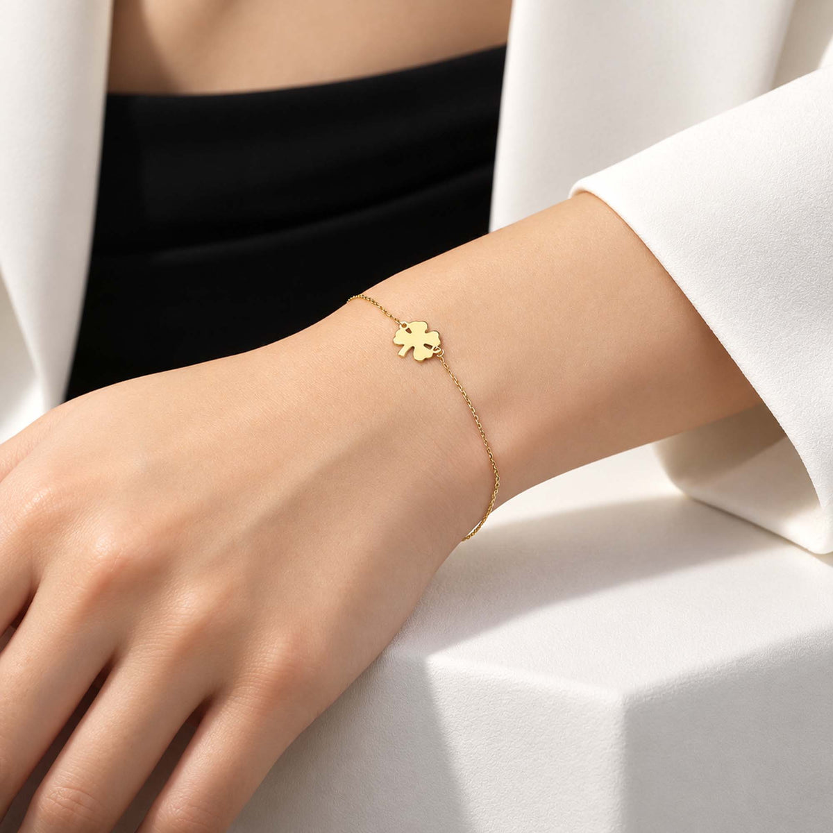 A person's wrist wearing a minimal clover bracelet in 14K yellow gold, with the bracelet centered on the wrist and visible against a white background.