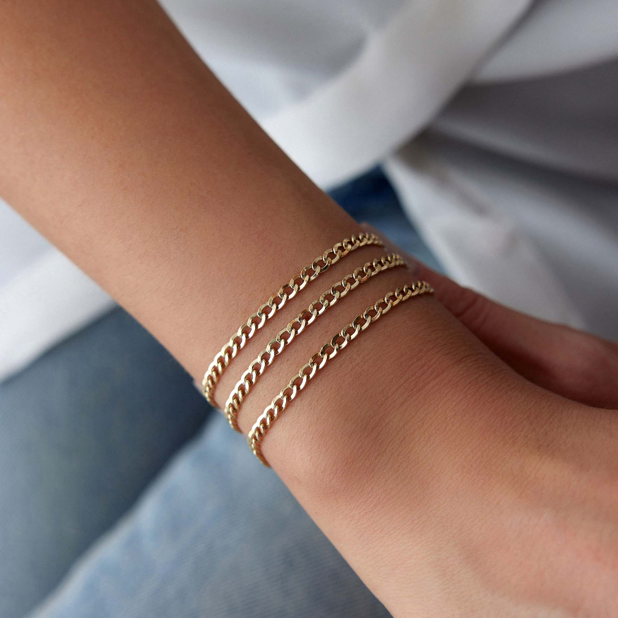 Minimal Gold curb chains bracelets on a person's wrist with a blurred background