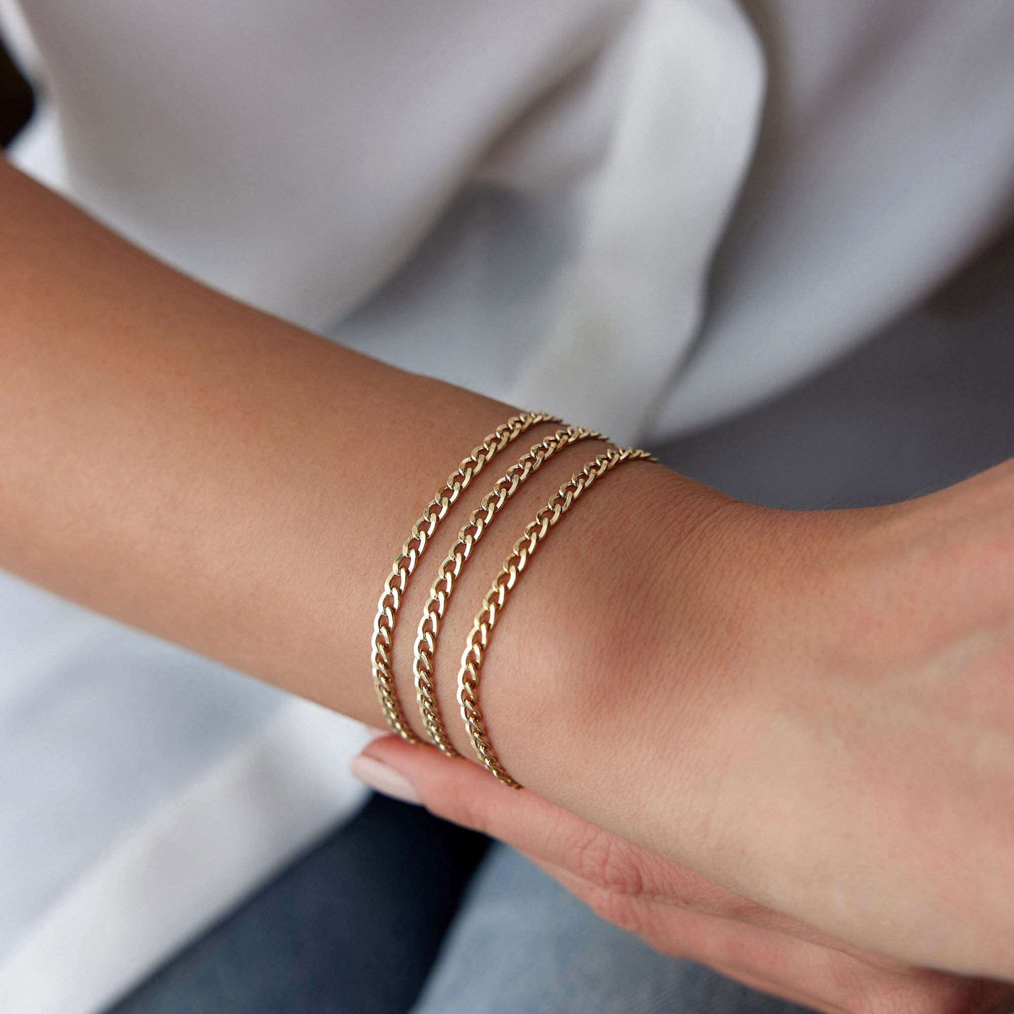 Minimal Gold curb chains bracelets on a person's wrist with a blurred background
