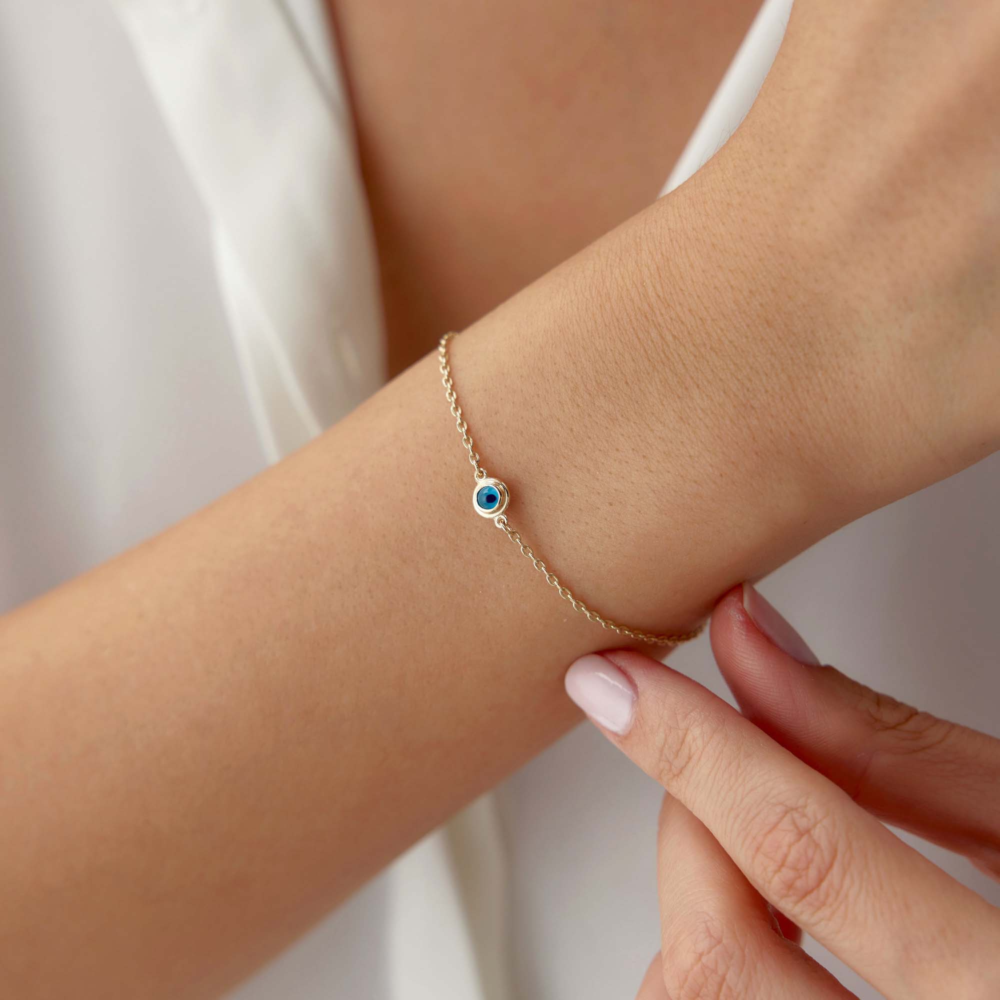 Gold bracelet with a blue evil eye on a wrist against a neutral background