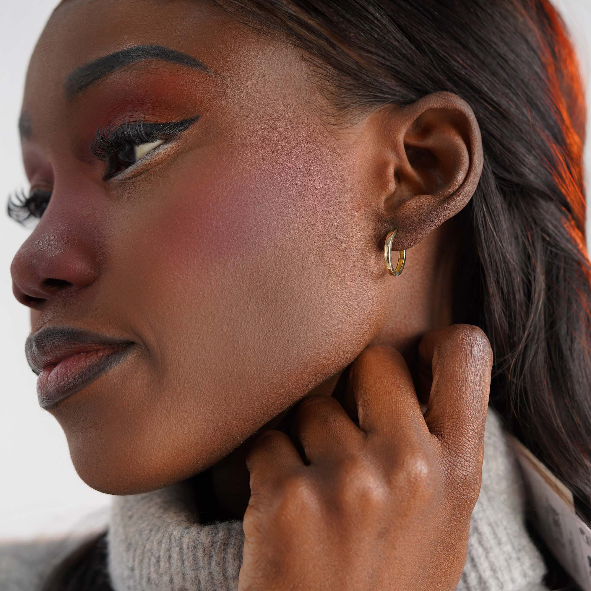 Close-up of a woman wearing an oval gold hoop earring against a neutral background