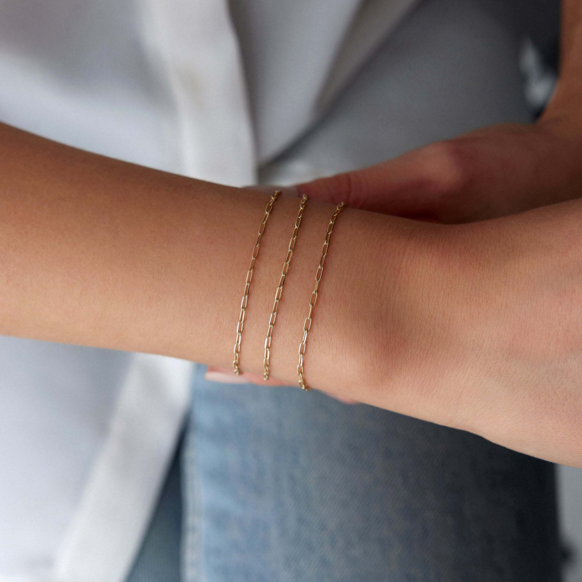 Minimal paperclip Gold chain bracelets on a wrist with a neutral background
