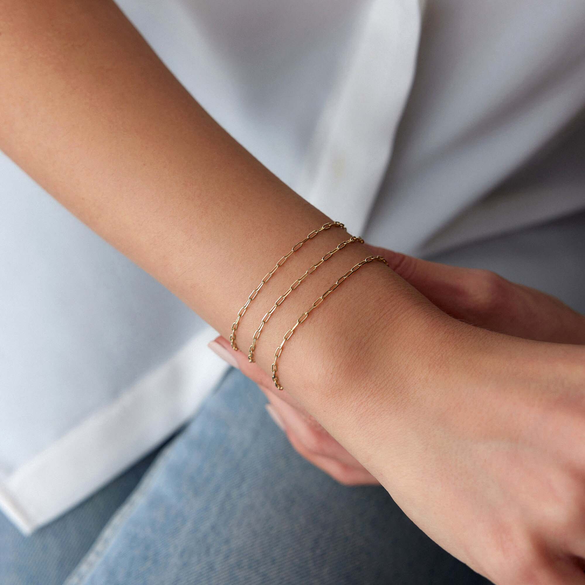 Minimal paperclip Gold chain bracelets on a wrist with a neutral background