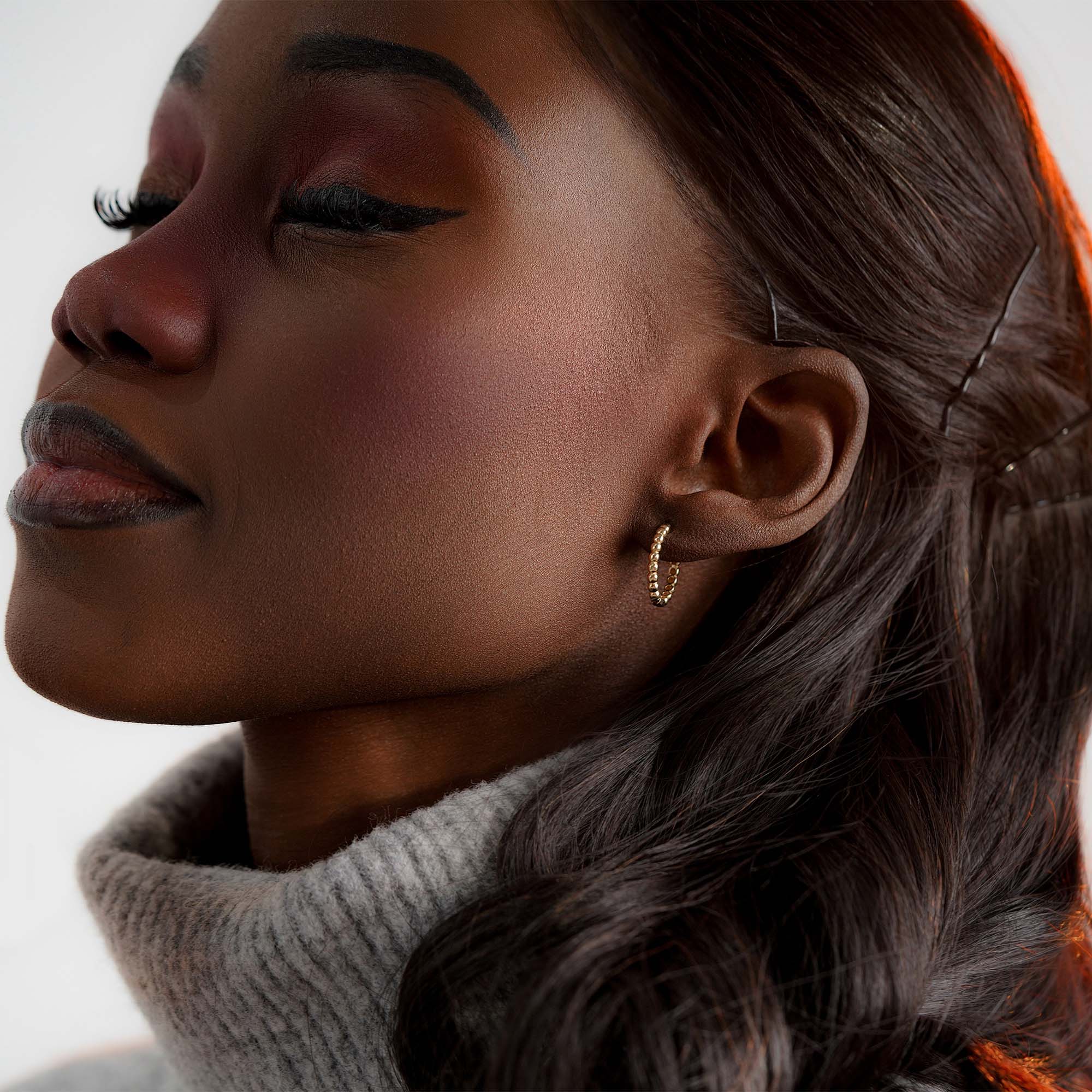 Close-up of a woman wearing a beaded gold earring with a neutral background