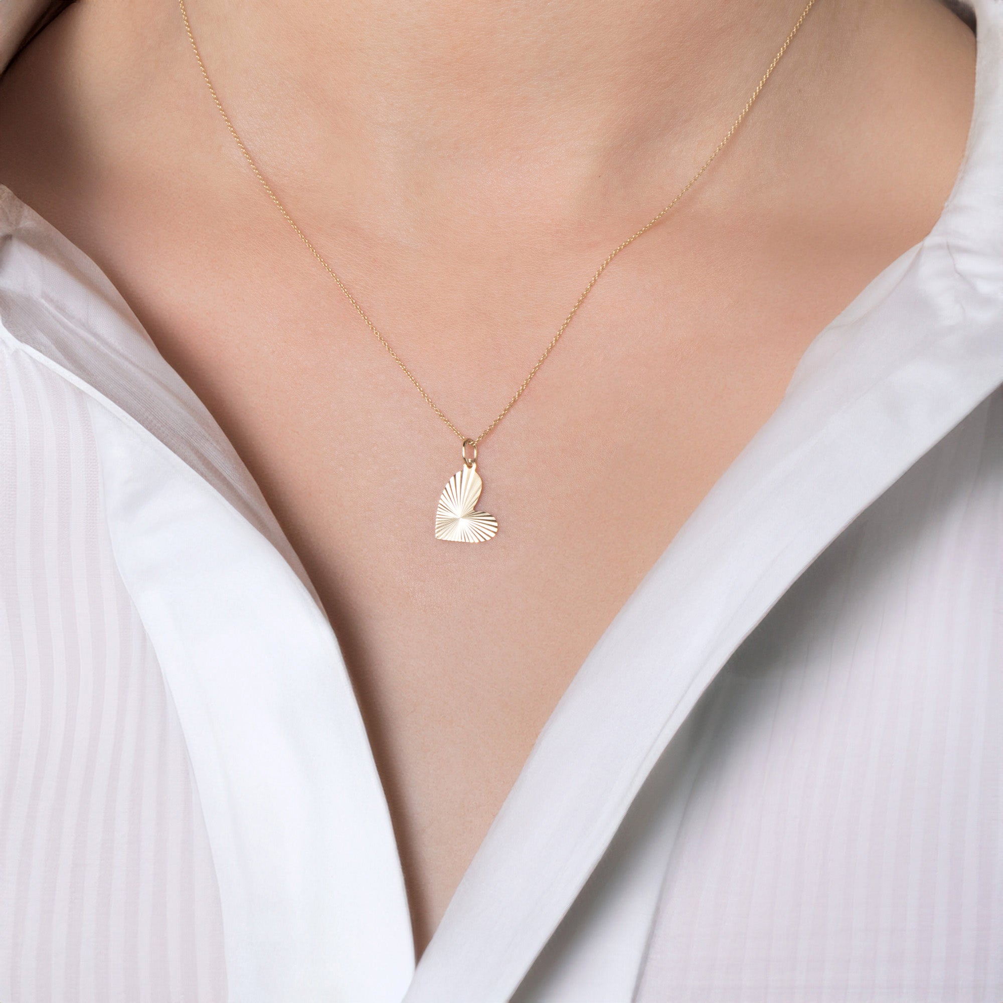 A person wearing a white shirt showcasing a 14K gold necklace with a heartburst pendant.