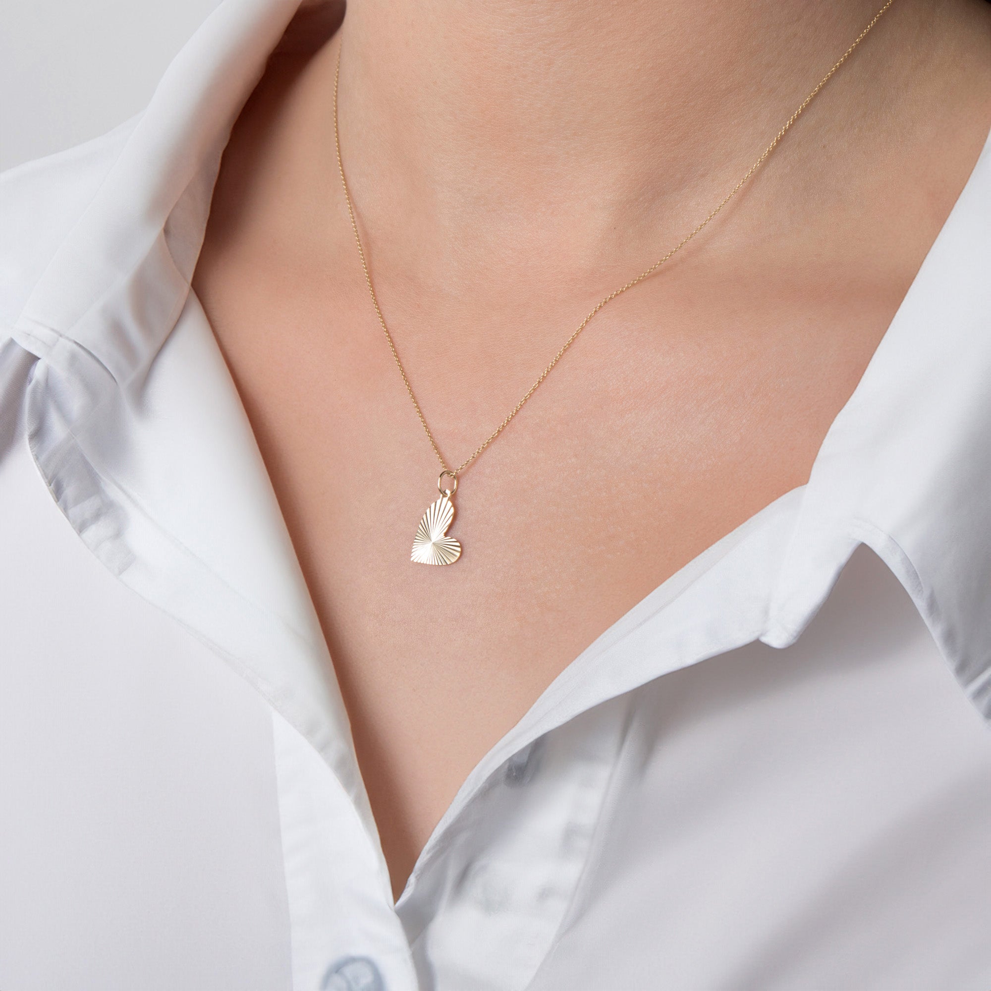 A person wearing a white shirt showcasing a 14K gold necklace with a heartburst pendant.