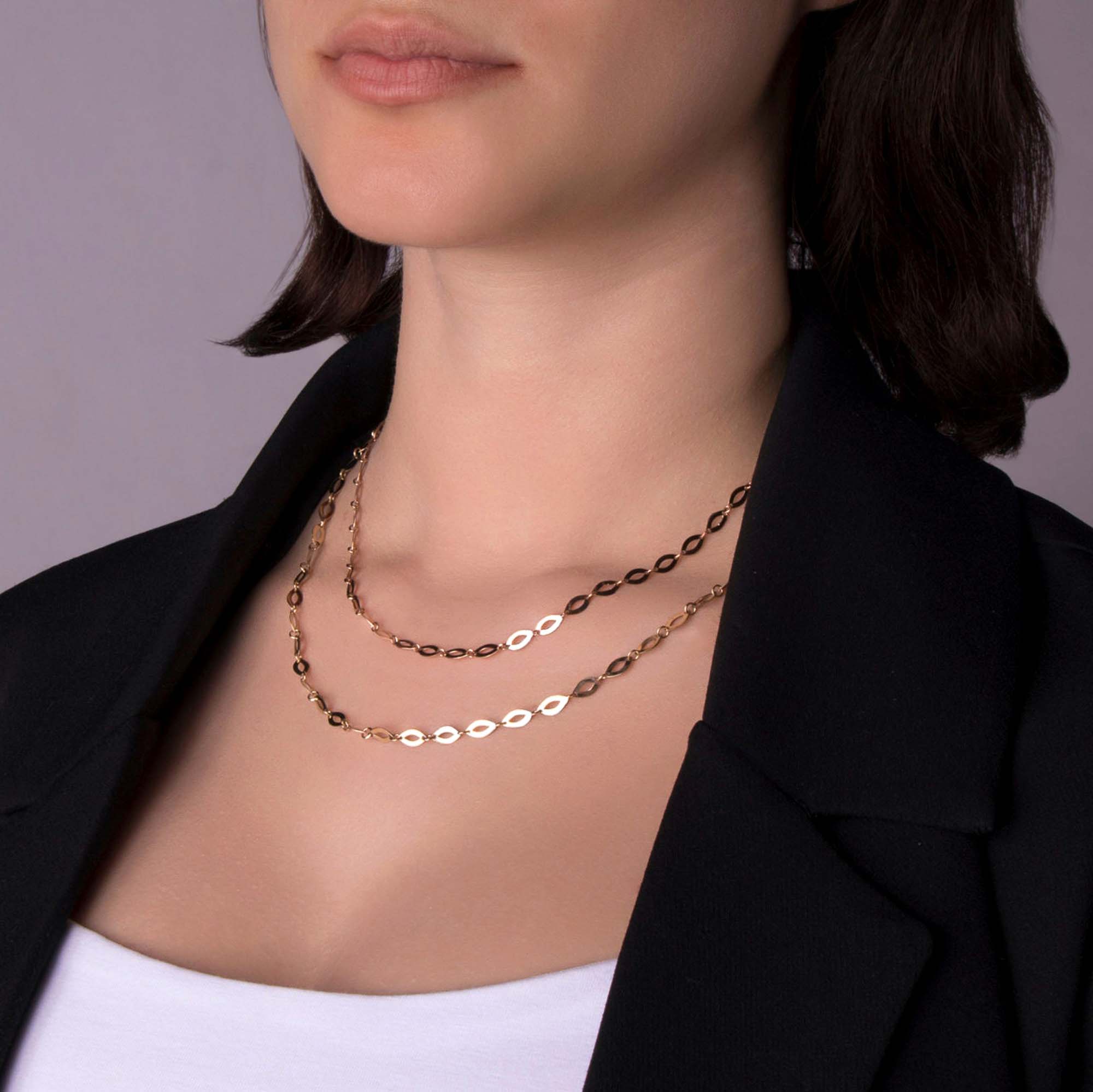 Close-up of a person wearing two oval mirror chain necklaces with a plain background