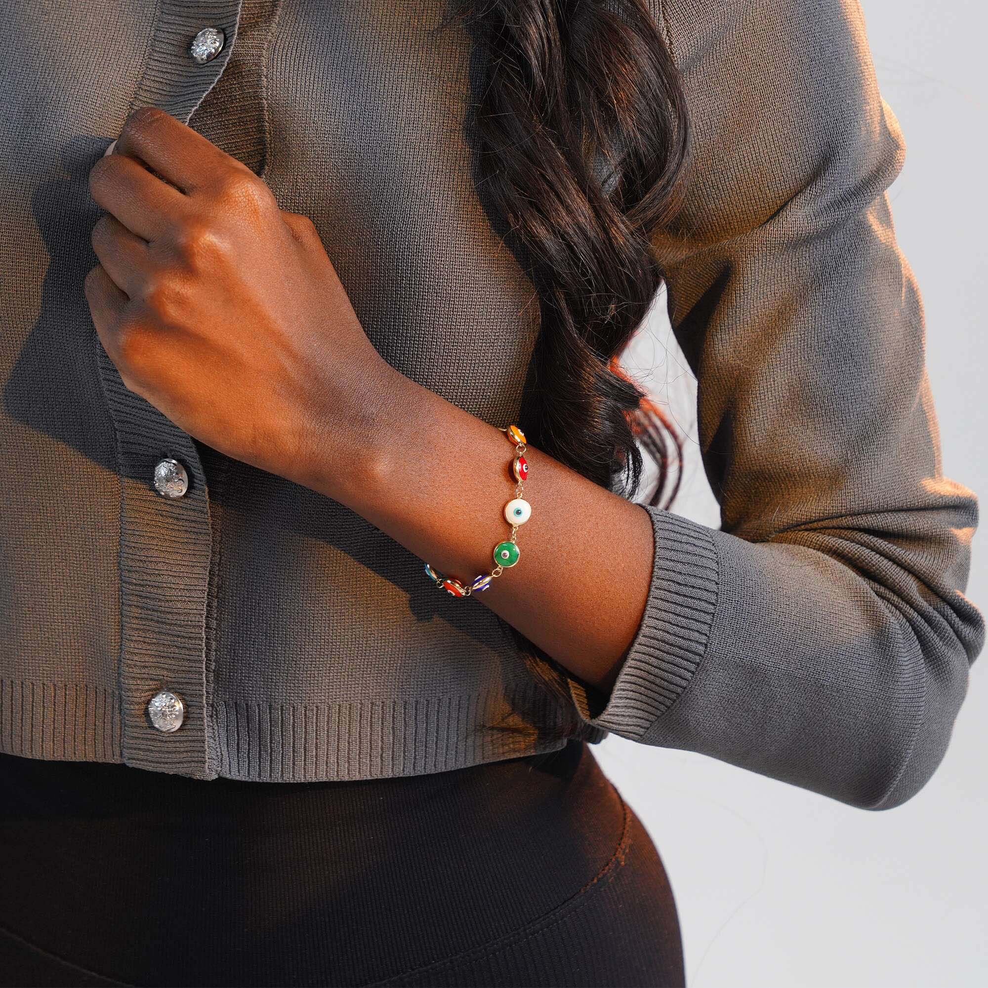 Person wearing a gray cardigan with a colorful evil eye bracelet on a neutral background