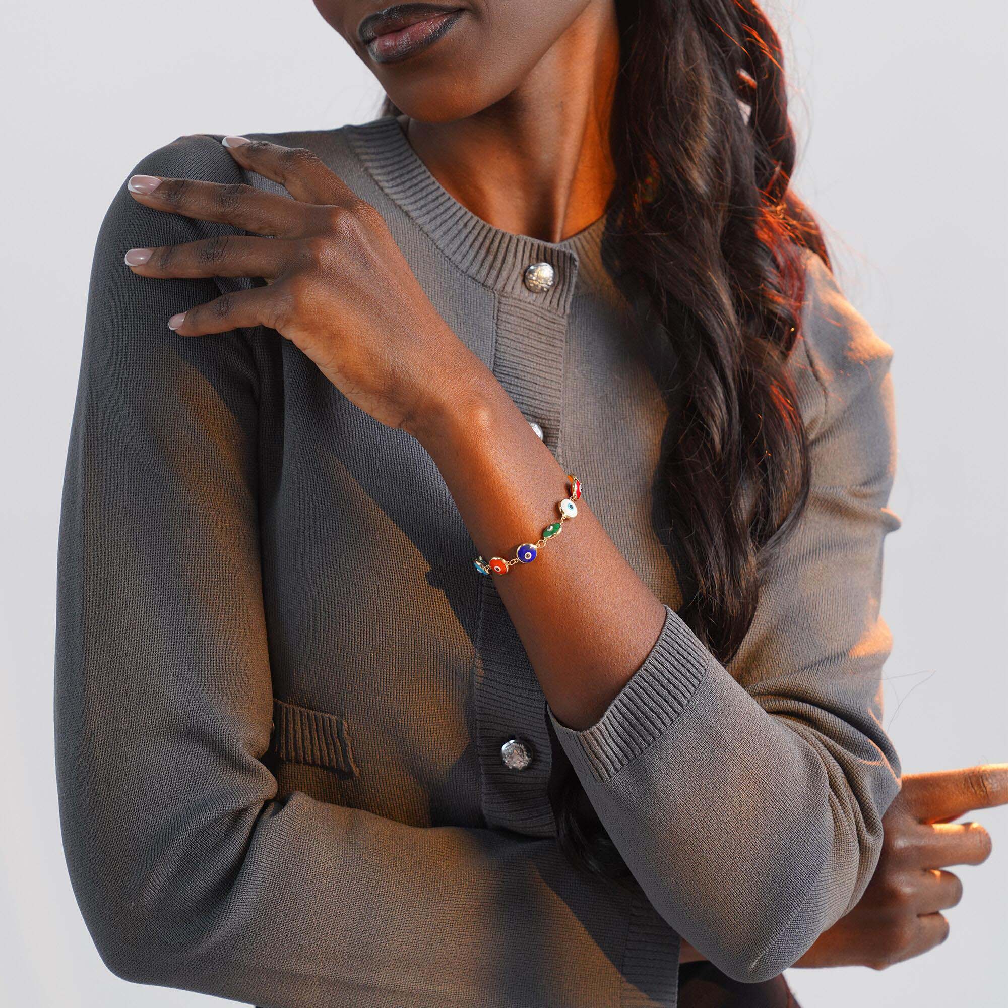 Woman wearing a gray sweater with colorful evil eye bracelet on a plain background