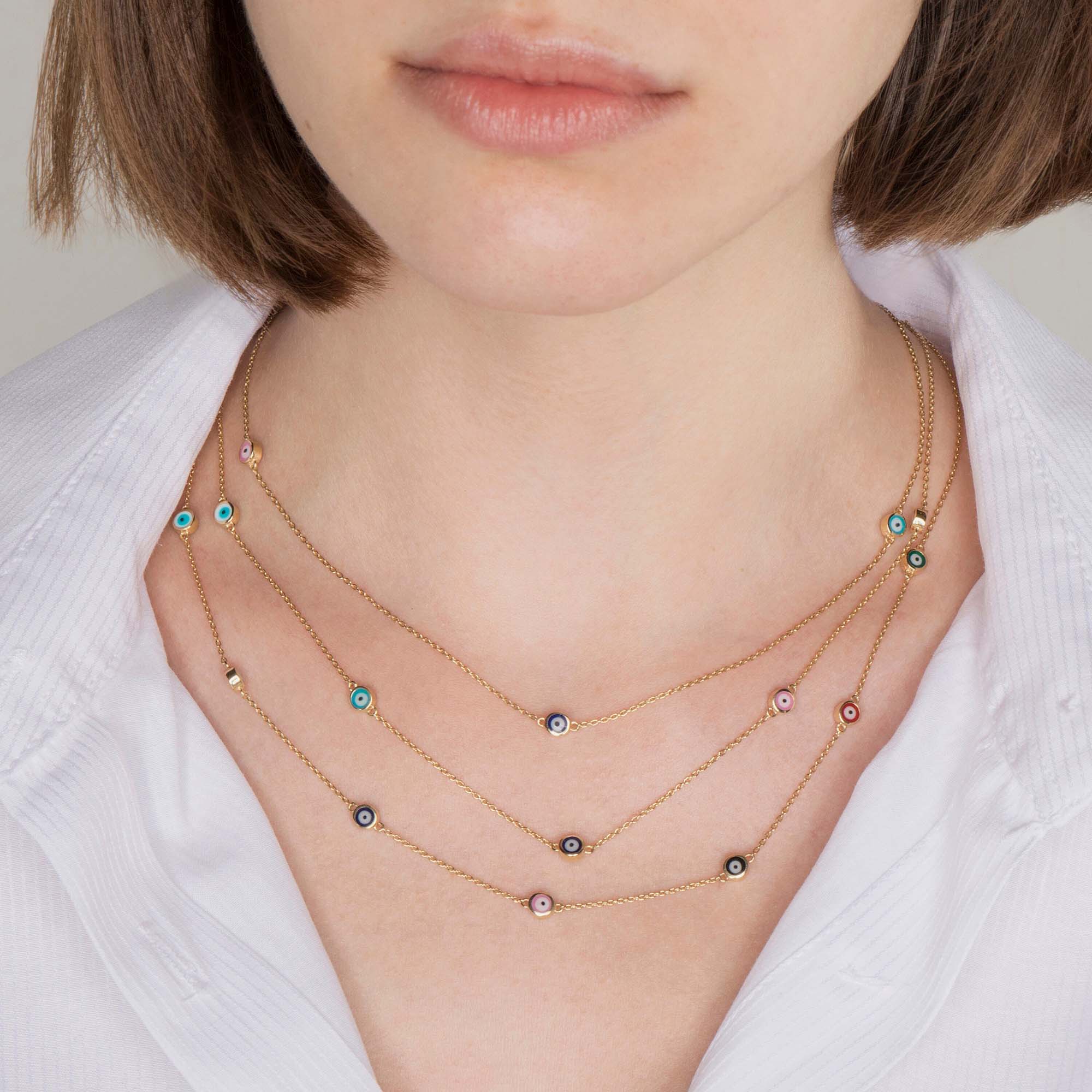 Close up of a model wearing 3 evil eye station necklaces. The first necklace features 3 multicolor evil eyes, the second necklace features 5 multicolor evil eyes, the third necklace features 7 multicolor evil eyes.
