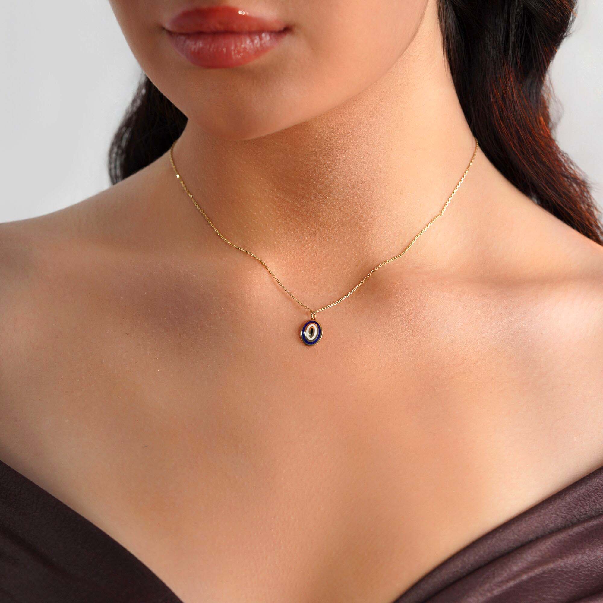 A model wearing an oval shaped 14k yellow gold evil eye pendant on a thin gold chain.