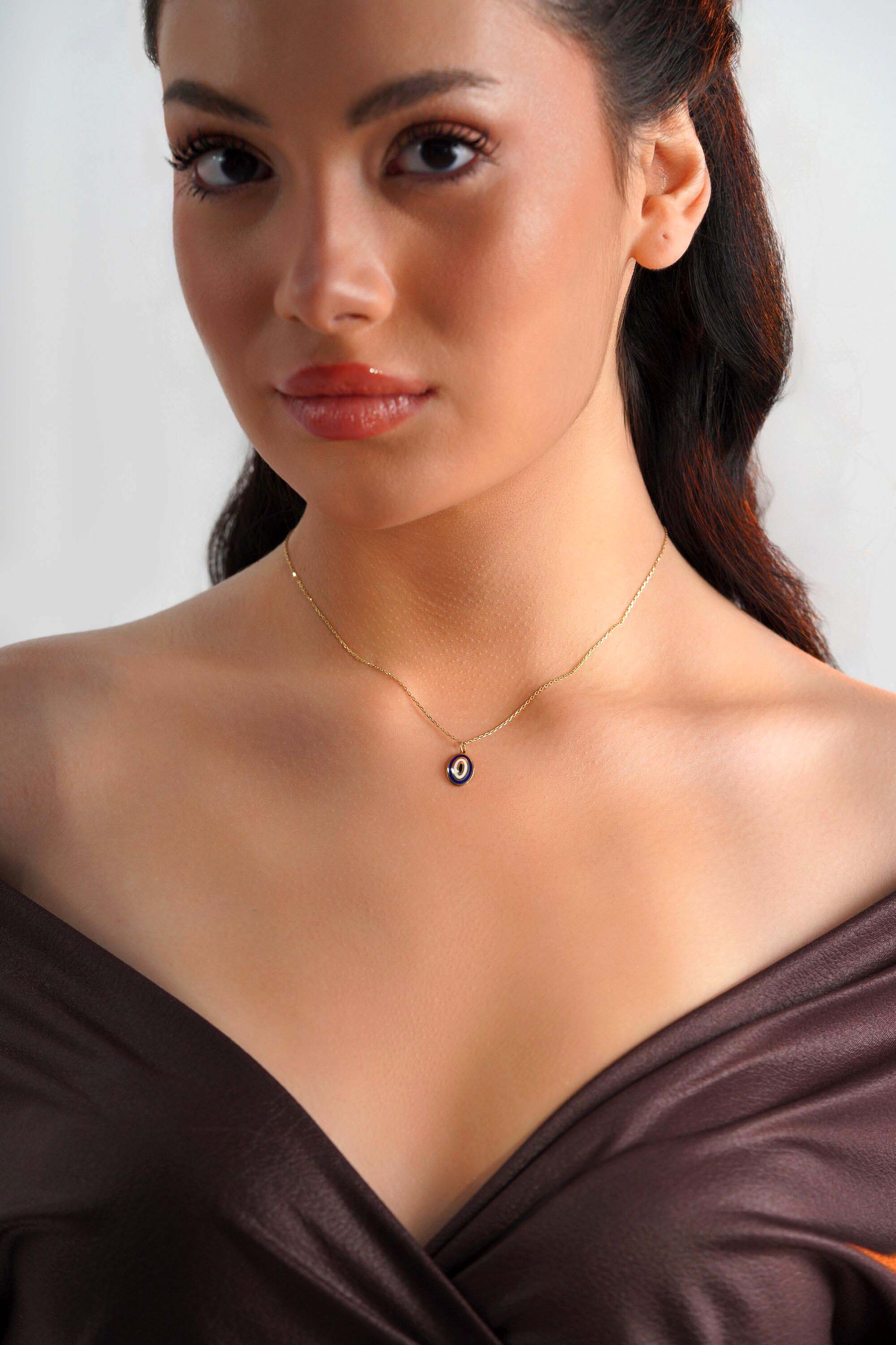 A model wearing an oval shaped 14k yellow gold evil eye pendant on a thin gold chain.