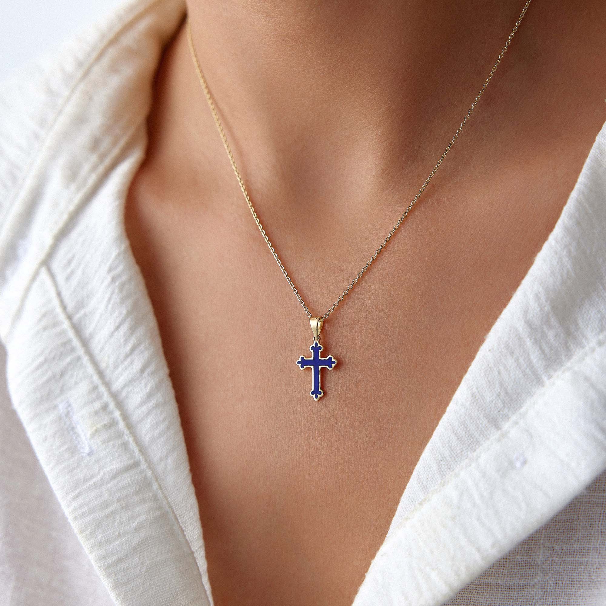 A 14k yellow gold small navy blue cross pendant worn on a thin gold chain.