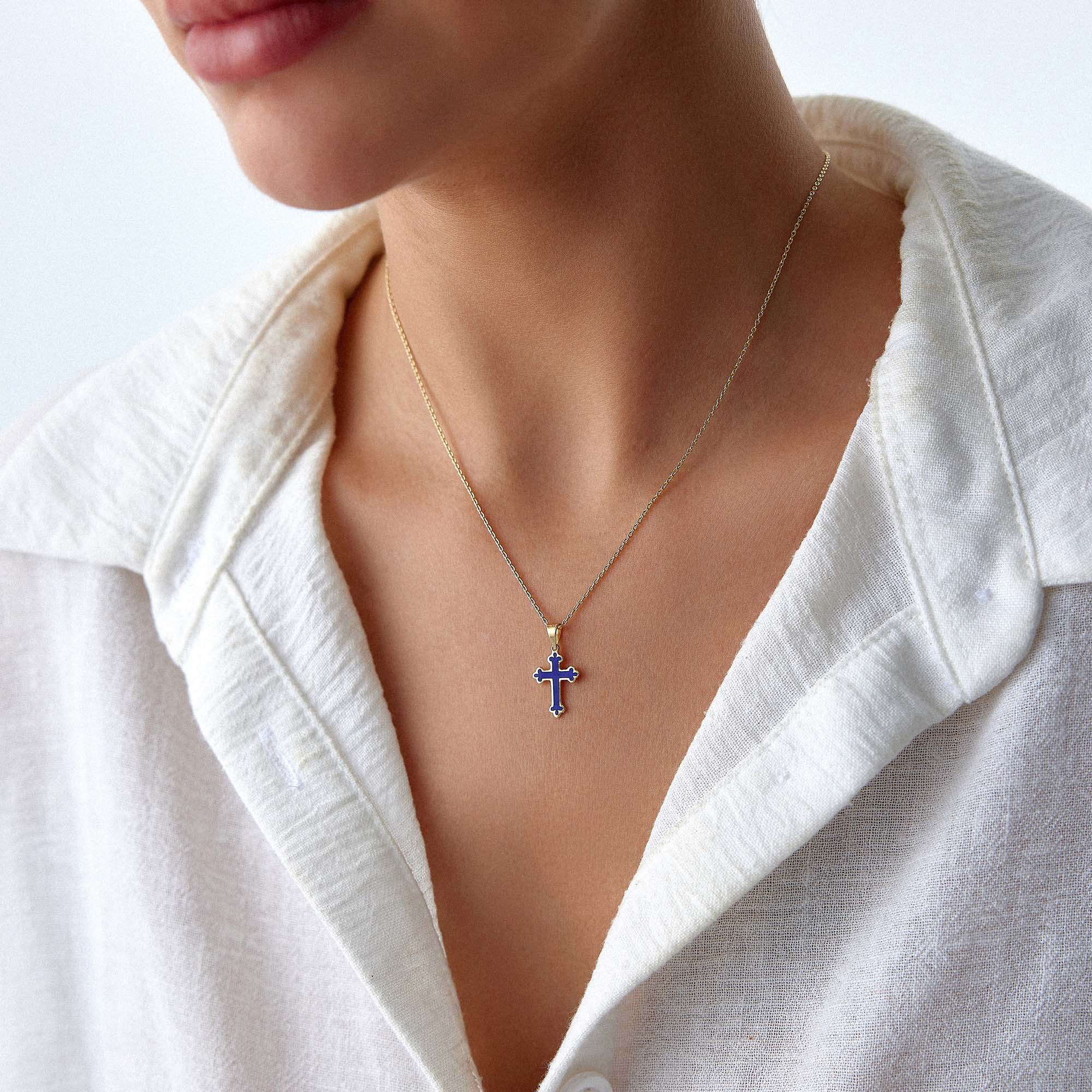 A 14k yellow gold small navy blue cross pendant worn on a thin gold chain.