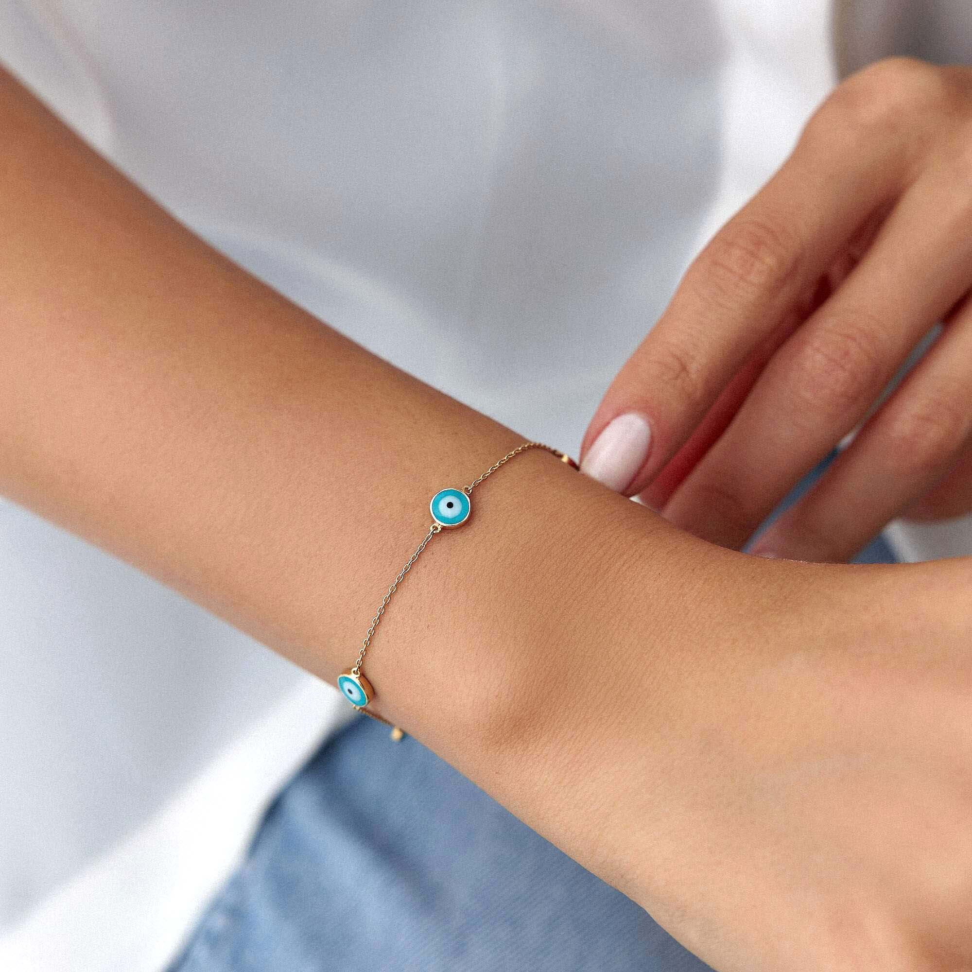 Close-up of a wrist wearing a bracelet with blue evil eyes on a plain background