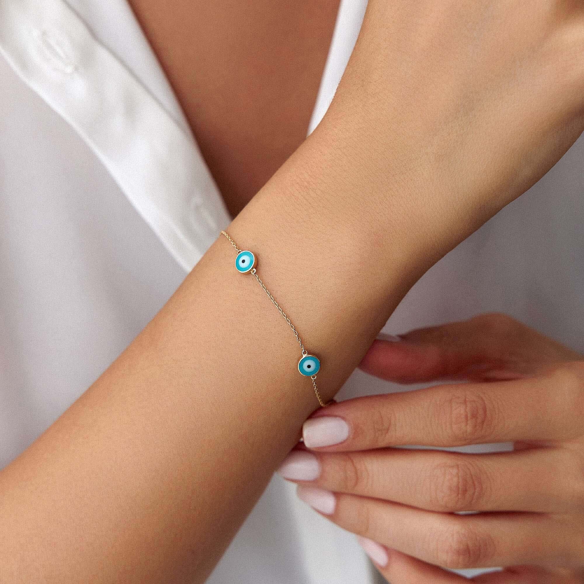 Close-up of a wrist wearing a bracelet with blue evil eyes on a plain background