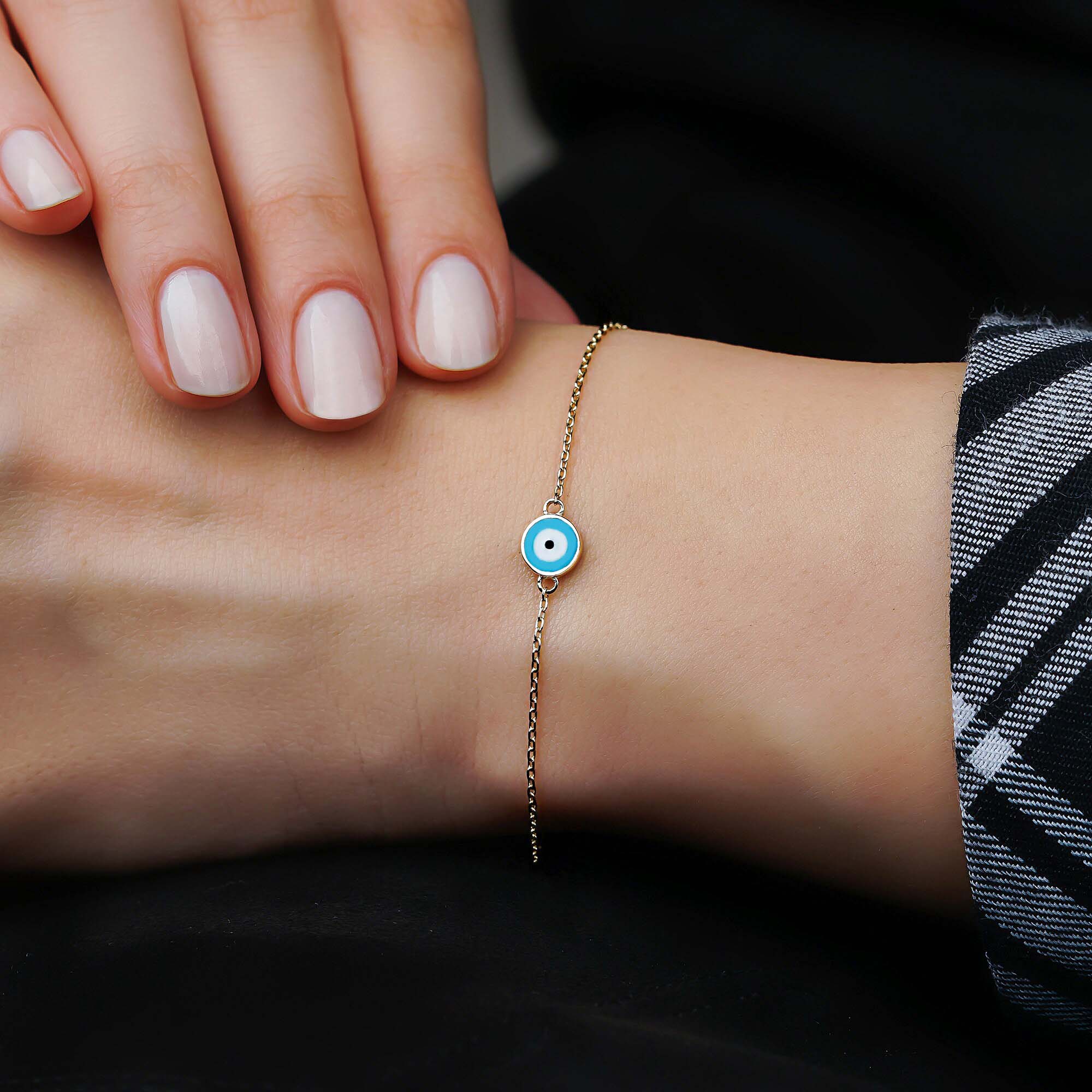 A 14k yellow gold ocean blue evil eye bracelet shown on a wrist.