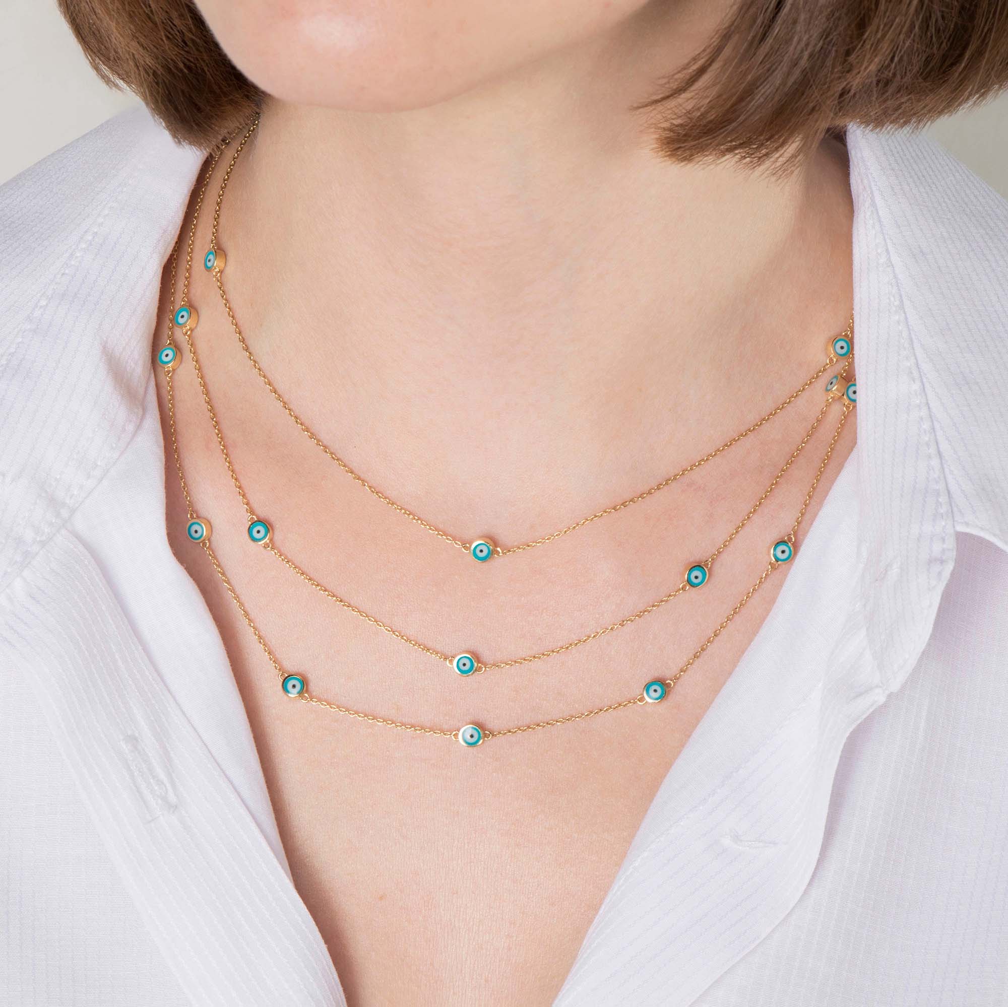 Three evil eye station necklaces shown layered up on a model. Top necklace features 3 ocean blue evil eyes, middle necklace features 5 ocean blue evil eyes, the bottom necklace features 7 ocean blue evil eyes.