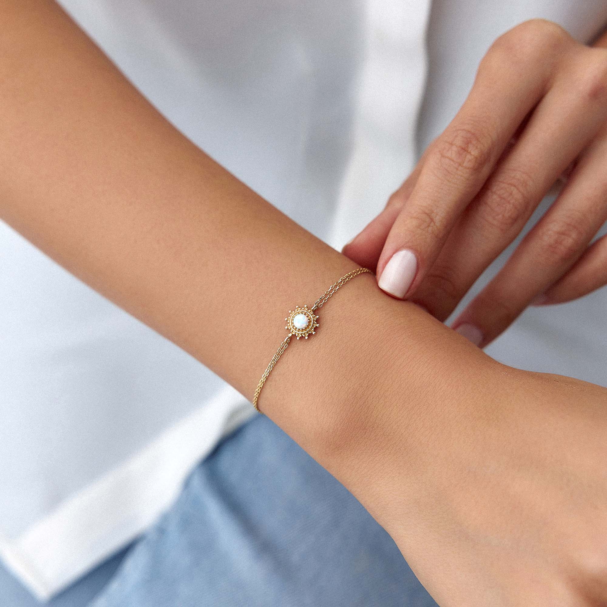 Gold bracelet with a central gemstone on a wrist against a white background