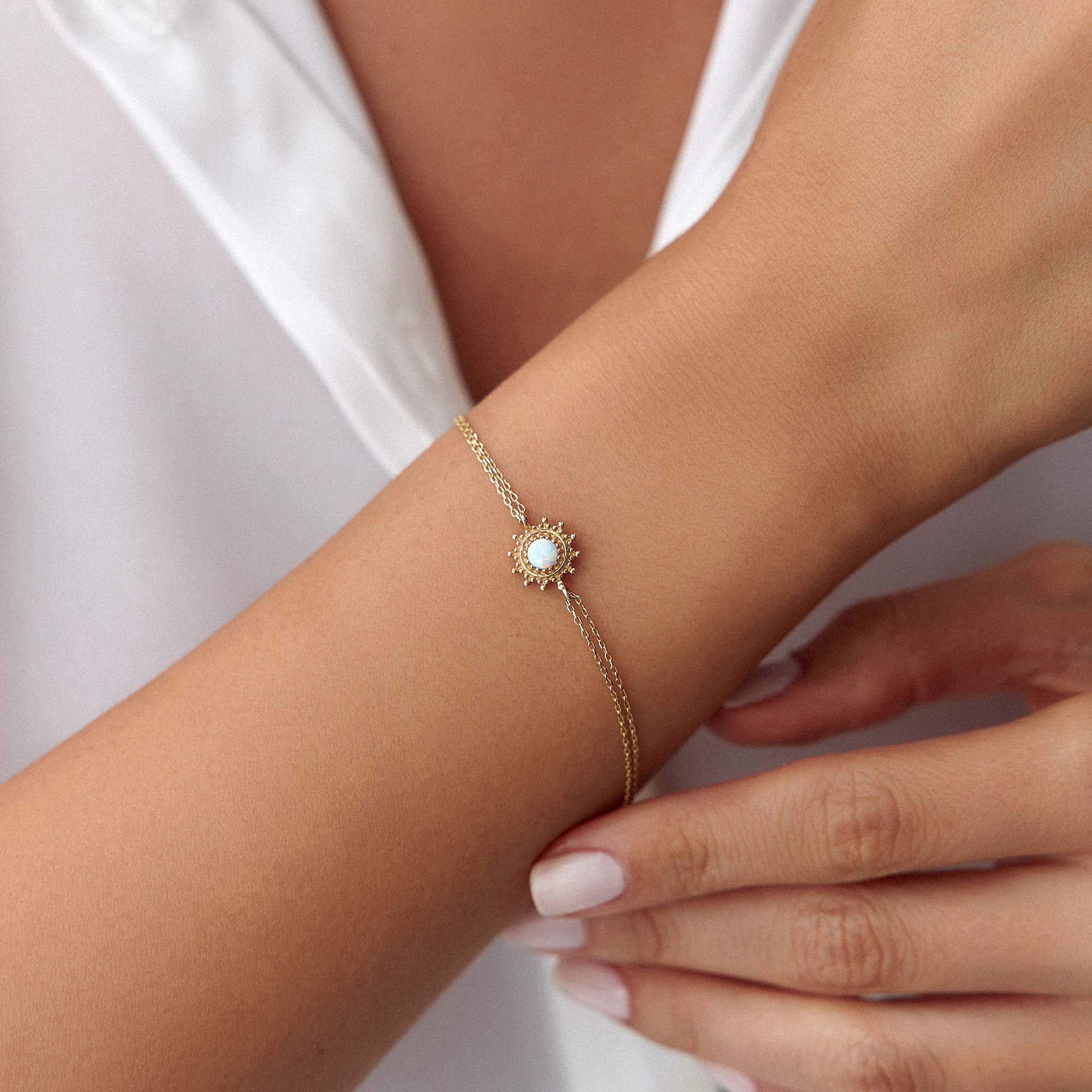 Gold bracelet with a central gemstone on a wrist against a white background