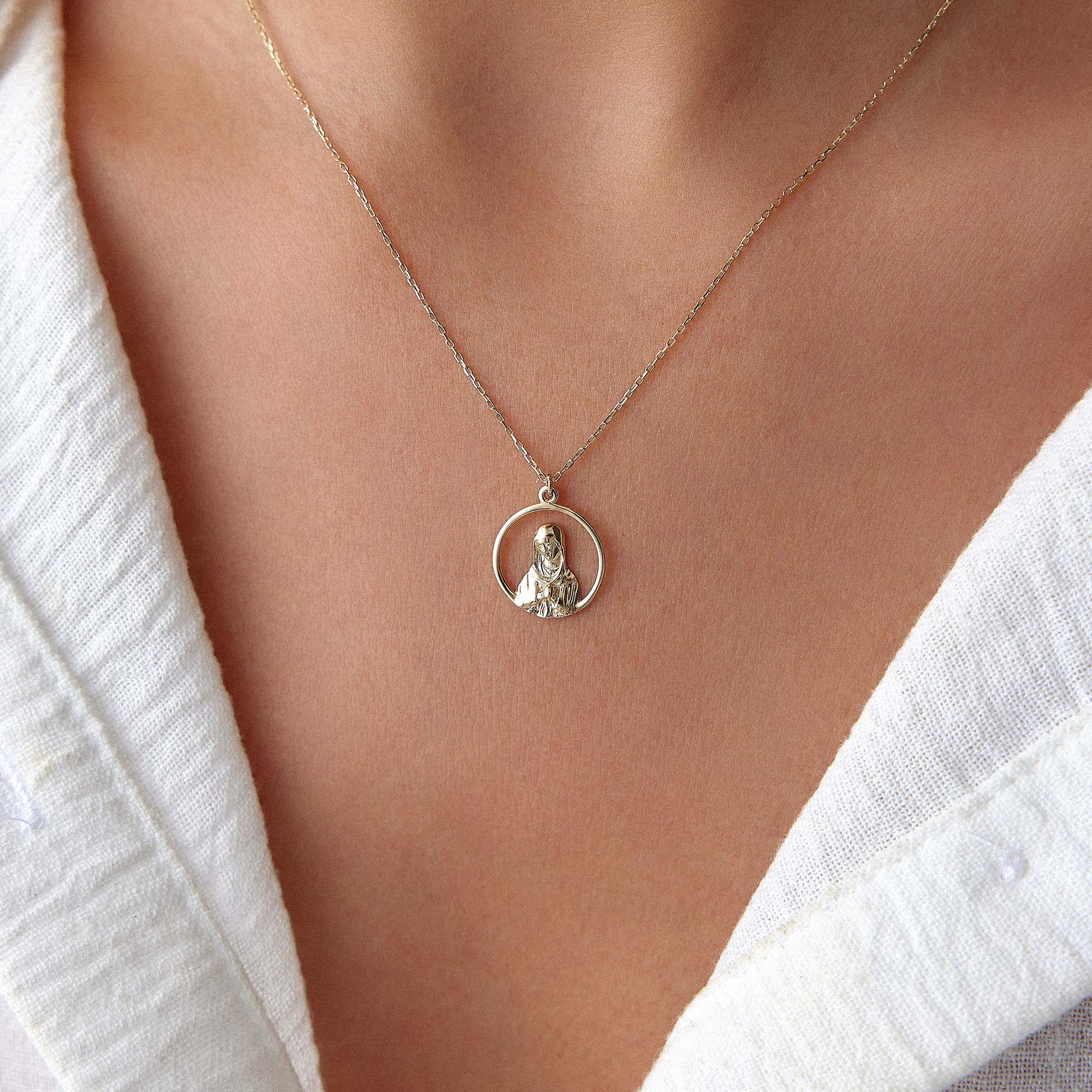 An upclose image of a model wearing an open virgin mary necklace