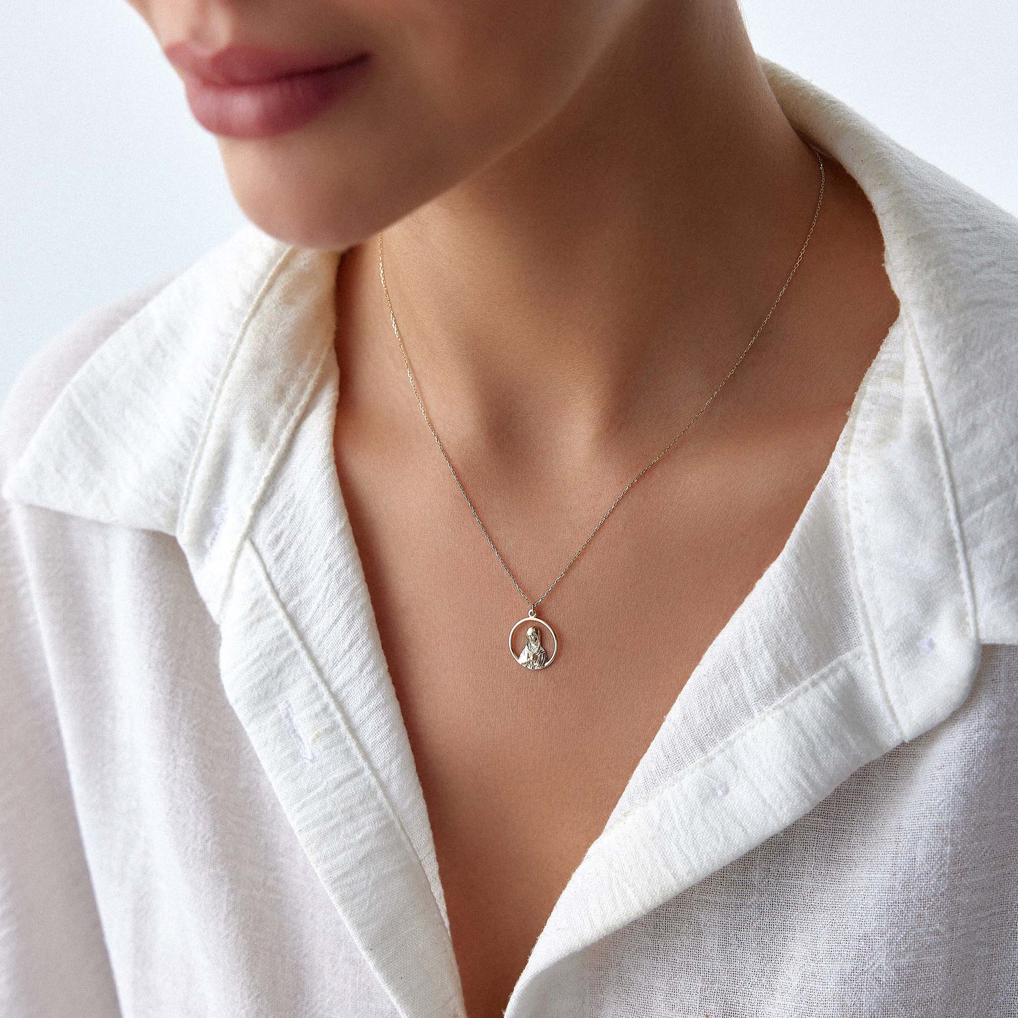 An upclose image of a model wearing an open virgin mary necklace