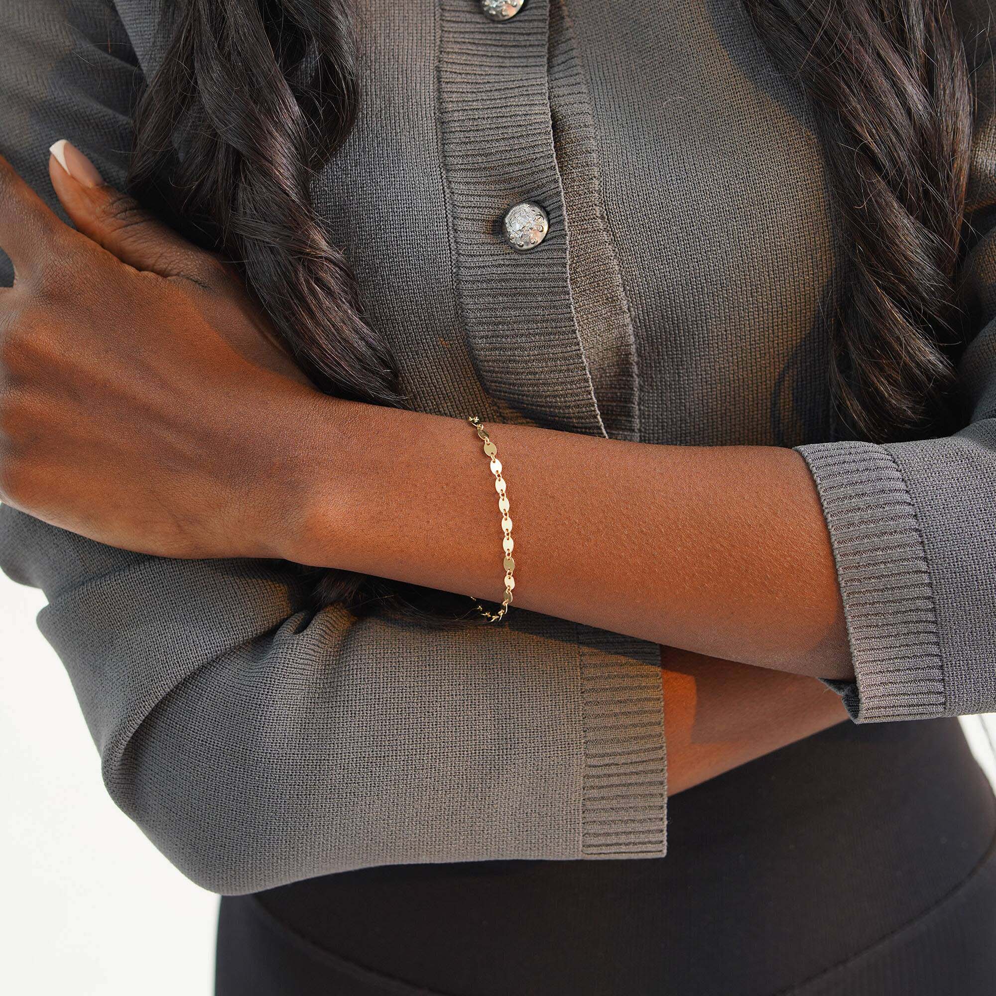 Person wearing a gold bracelet with a neutral background