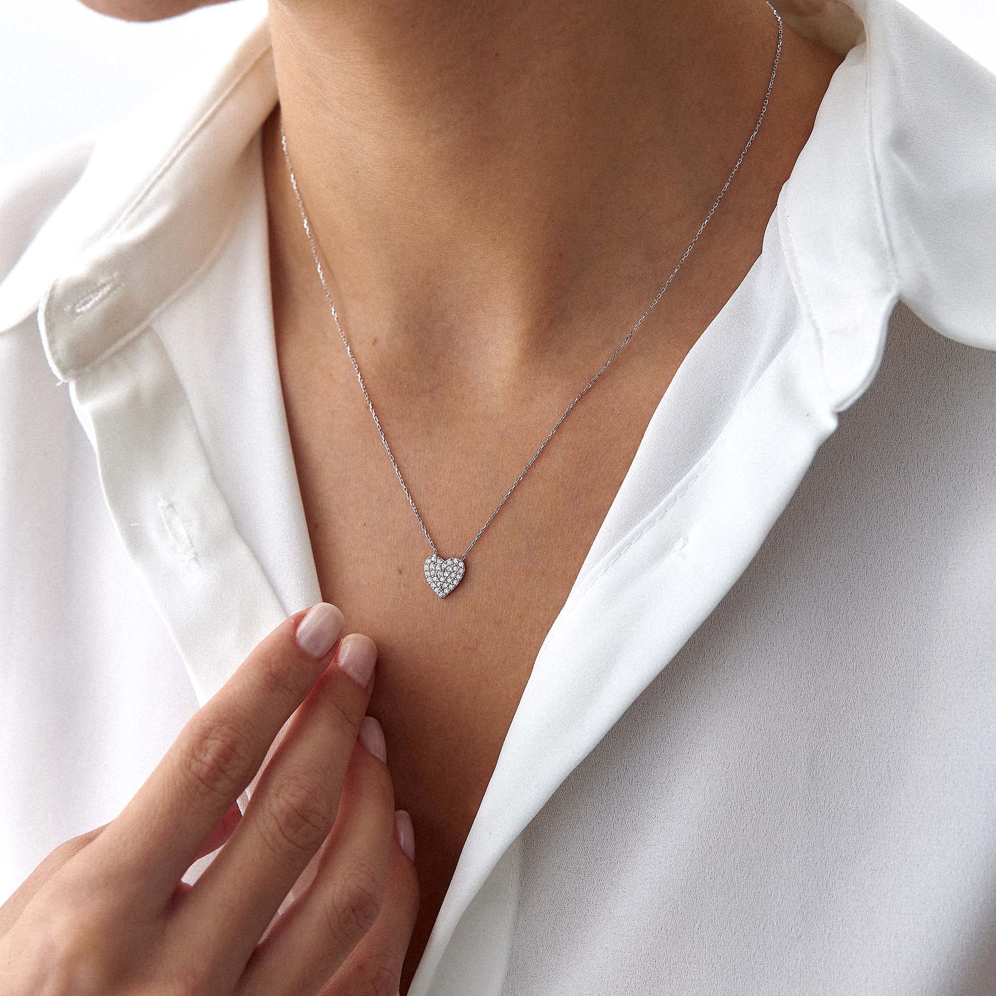 A minimal pave set heart-shaped necklace worn by a person in a white shirt