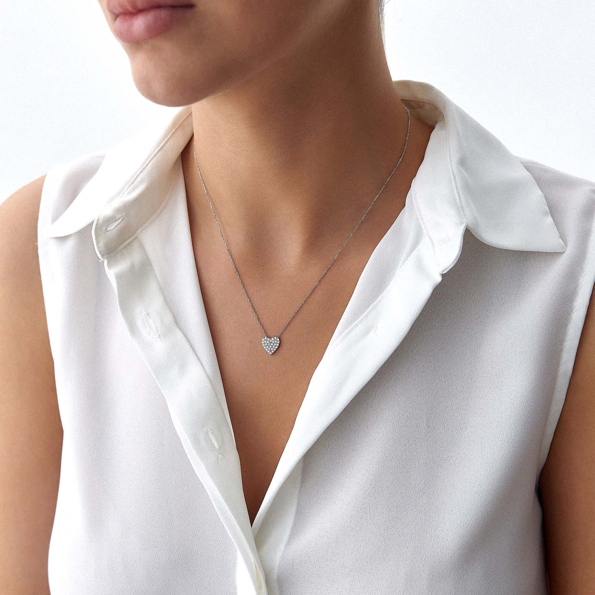 A minimal pave set heart-shaped necklace worn by a person in a white shirt