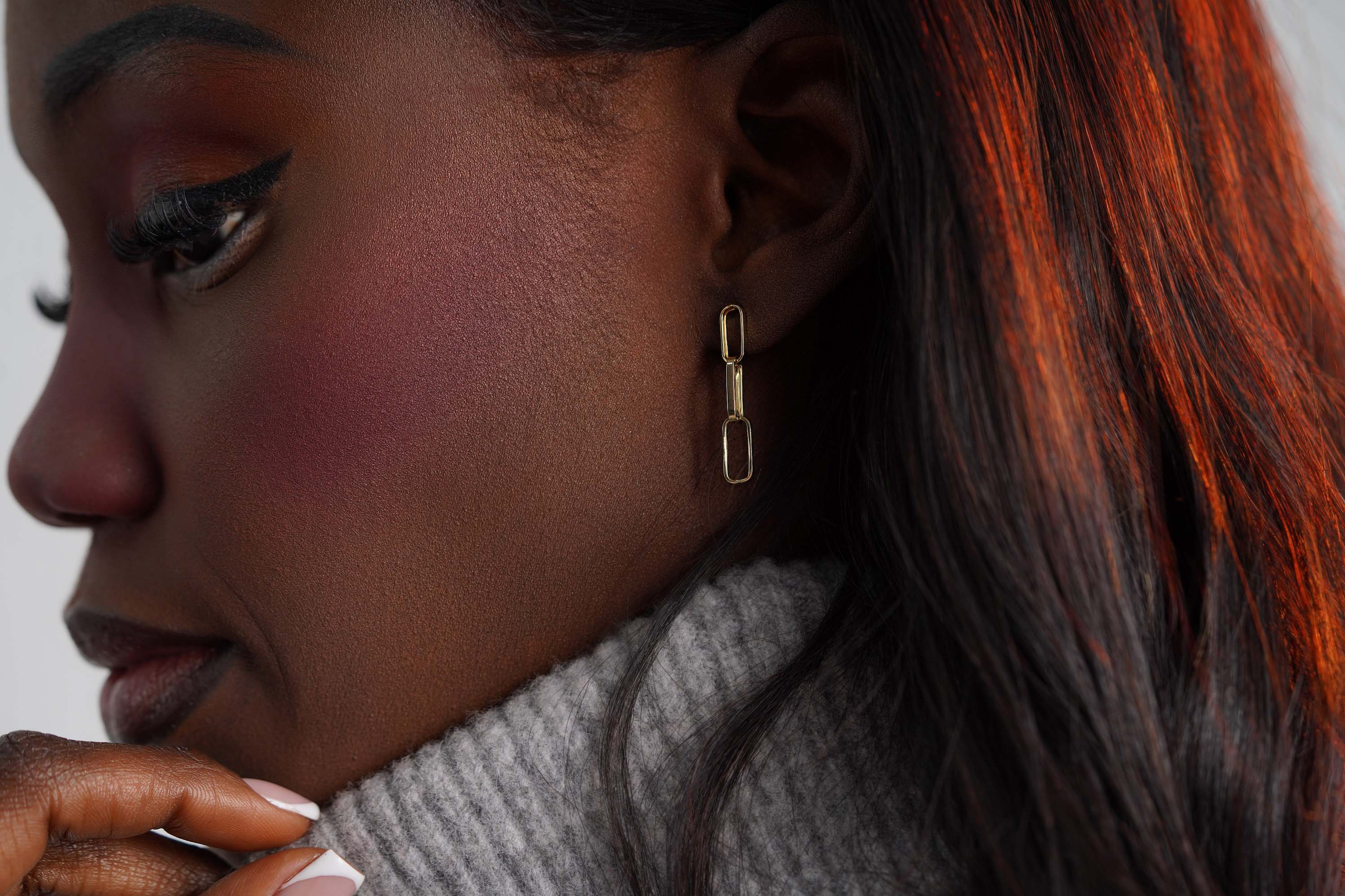 A 14k yellow gold paperclip chain stud worn on an ear.