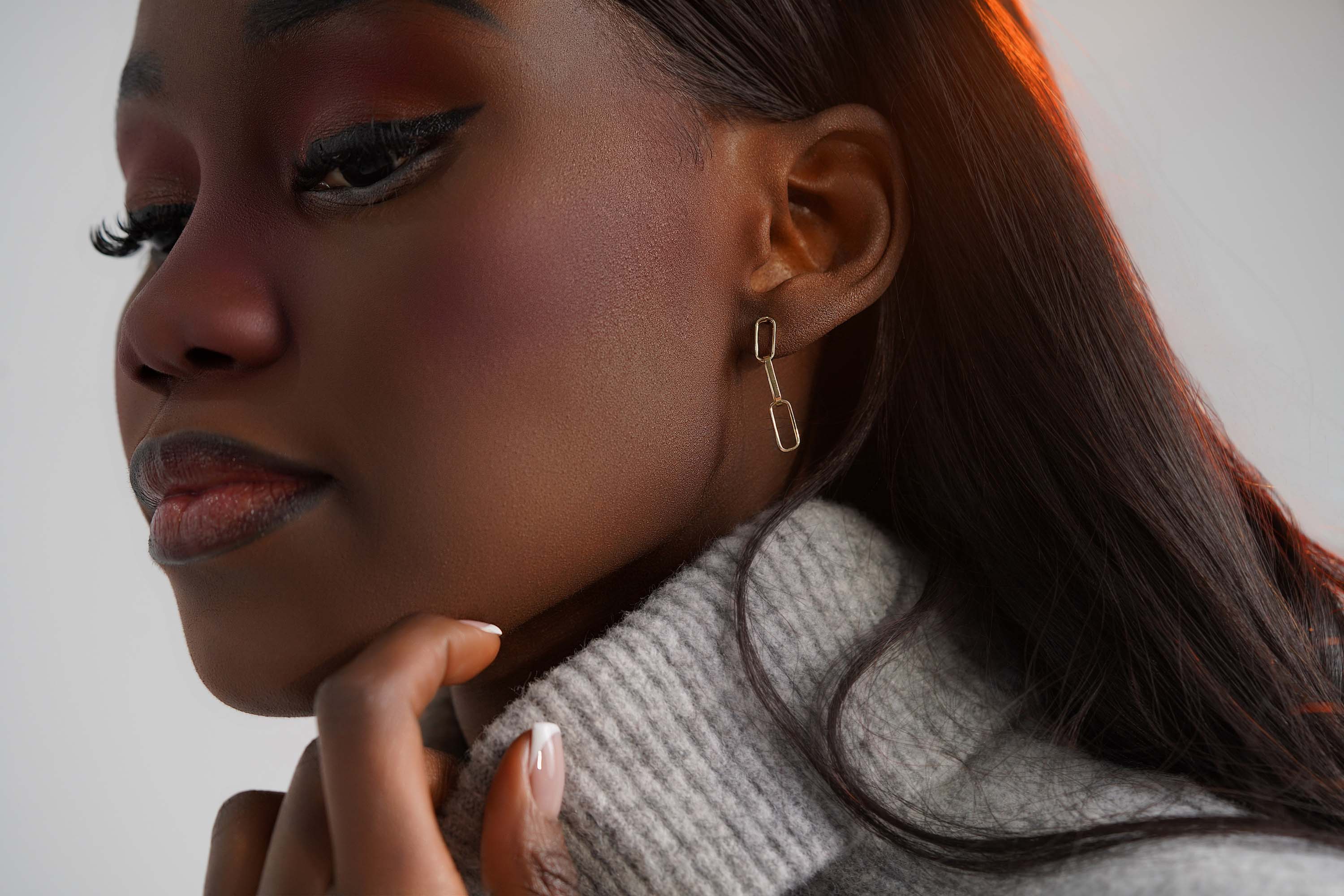 A 14k yellow gold paperclip chain stud worn on an ear.