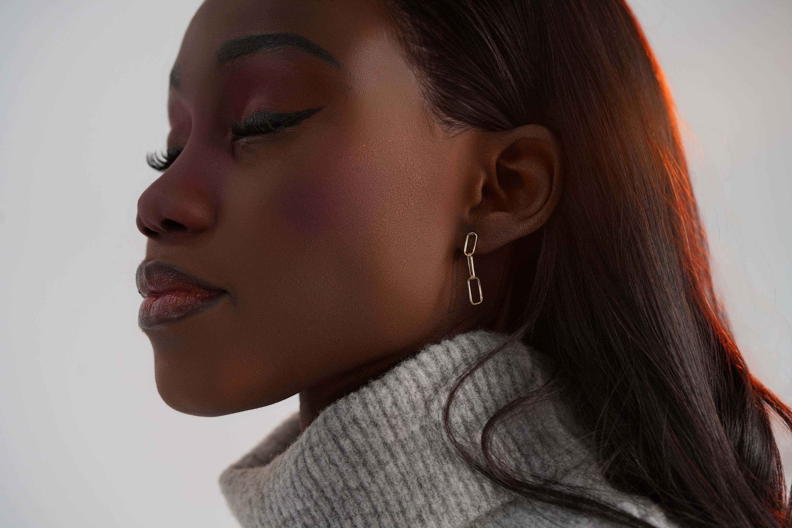 A 14k yellow gold paperclip chain stud worn on an ear.