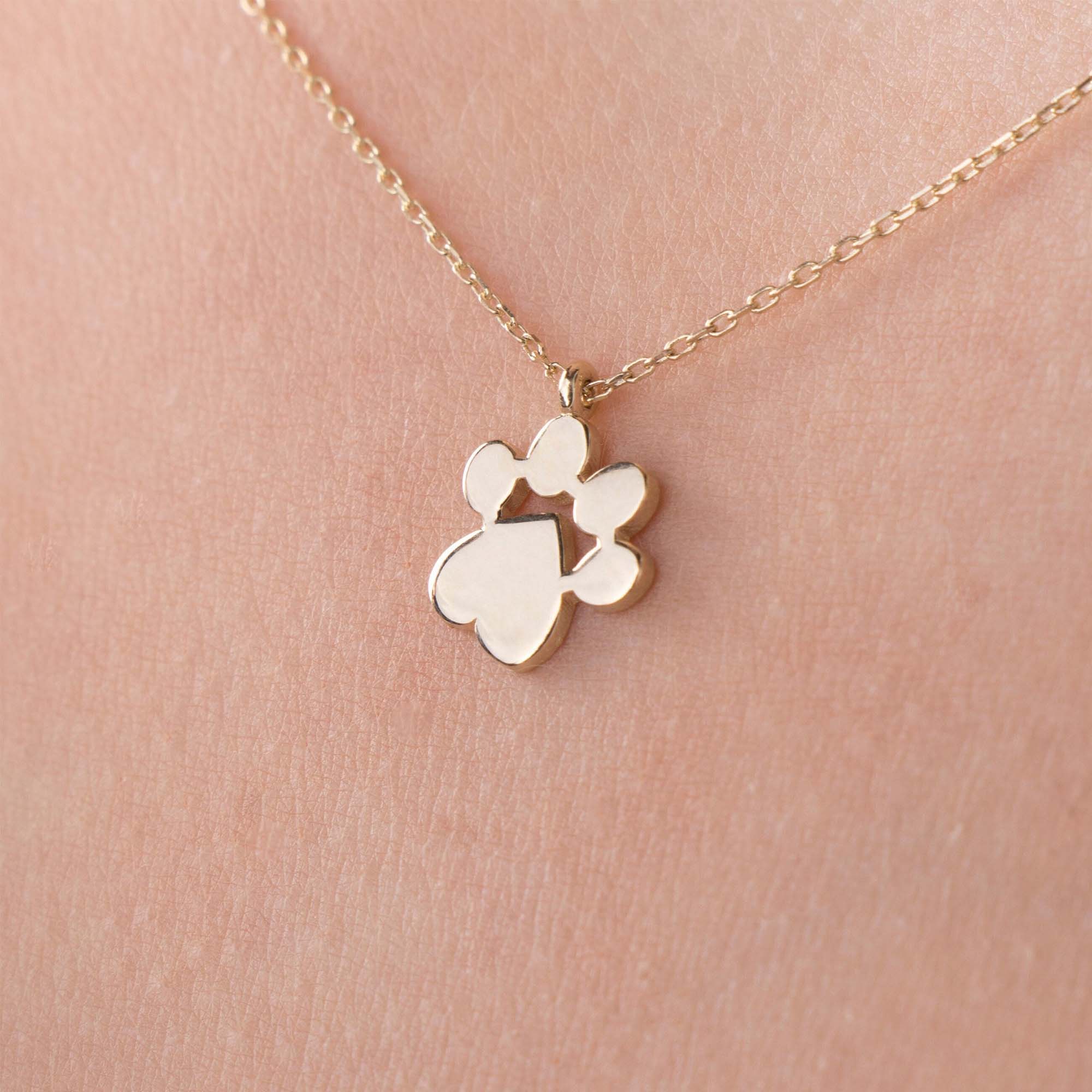 Gold necklace with a paw print pendant on a person's neck against a pink background