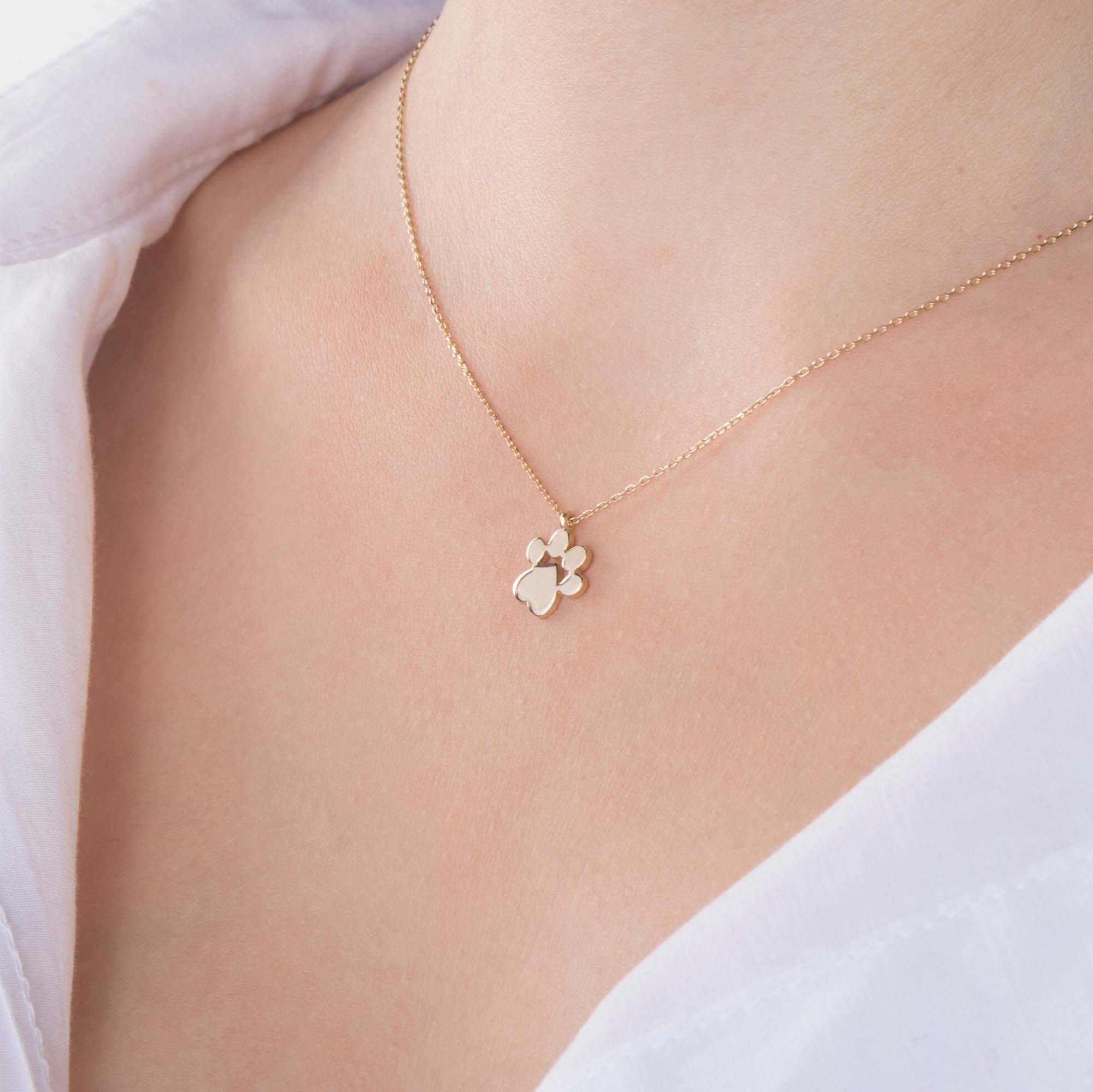 Gold necklace with a paw print pendant on a person wearing a white shirt.