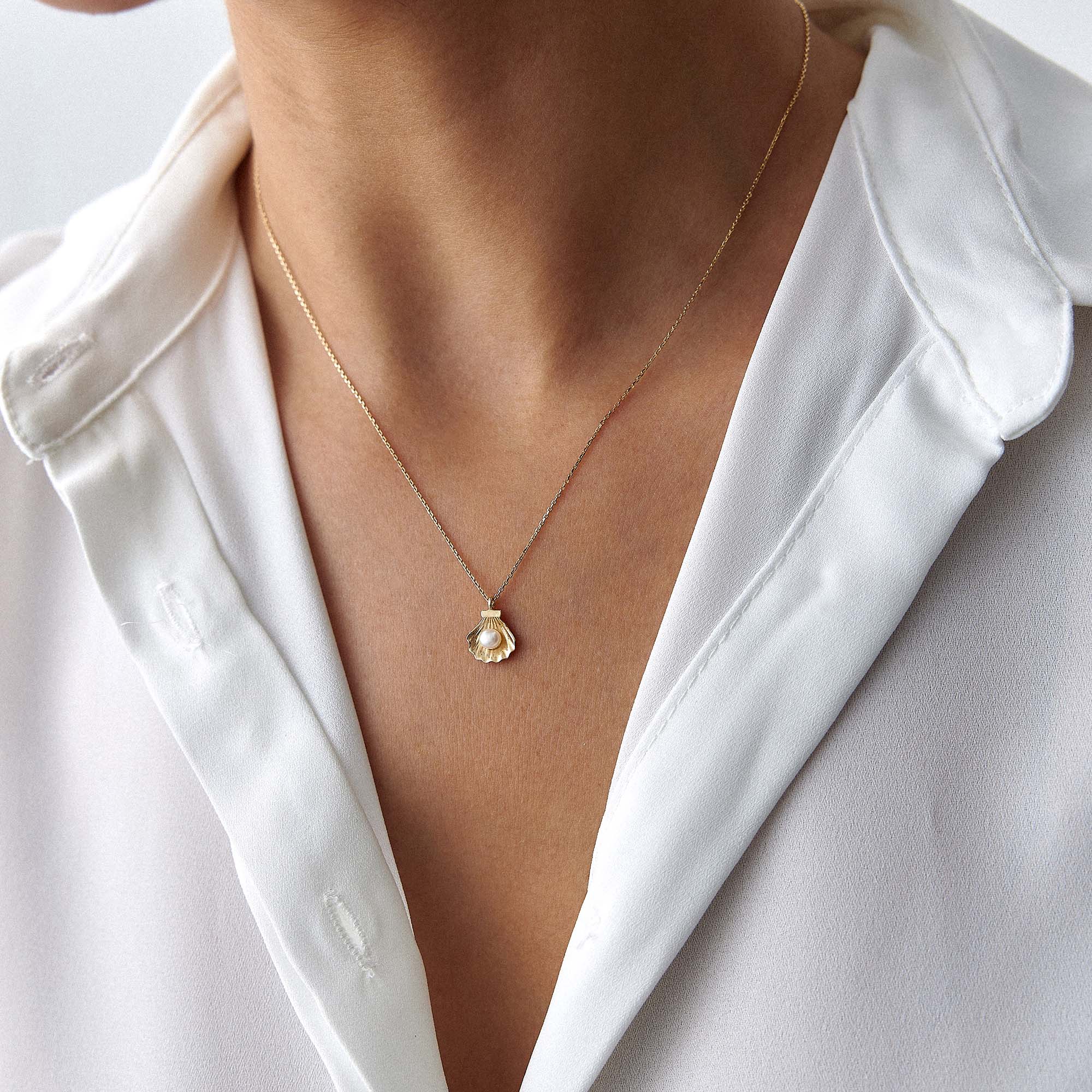 A model wearing a delicate gold necklace with a pearl shell and a pearl at its center