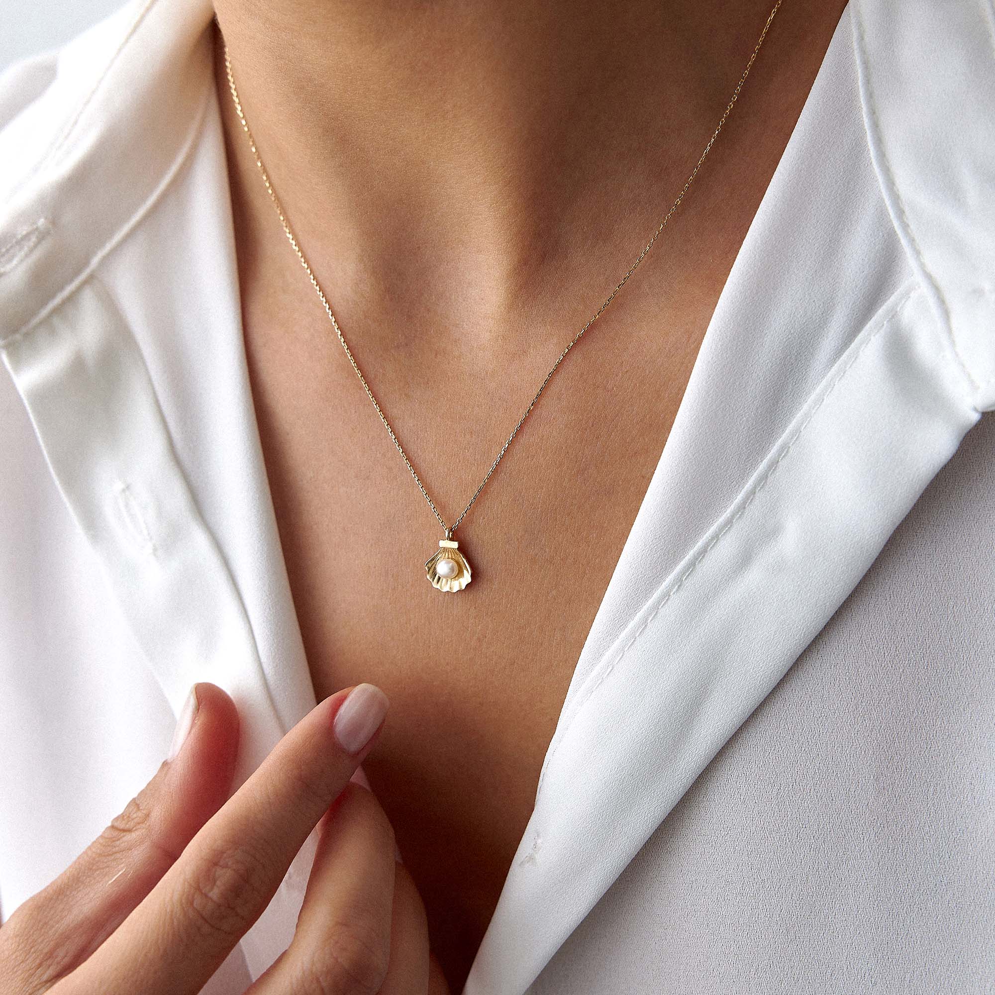 A model wearing a delicate gold necklace with a pearl shell and a pearl at its center