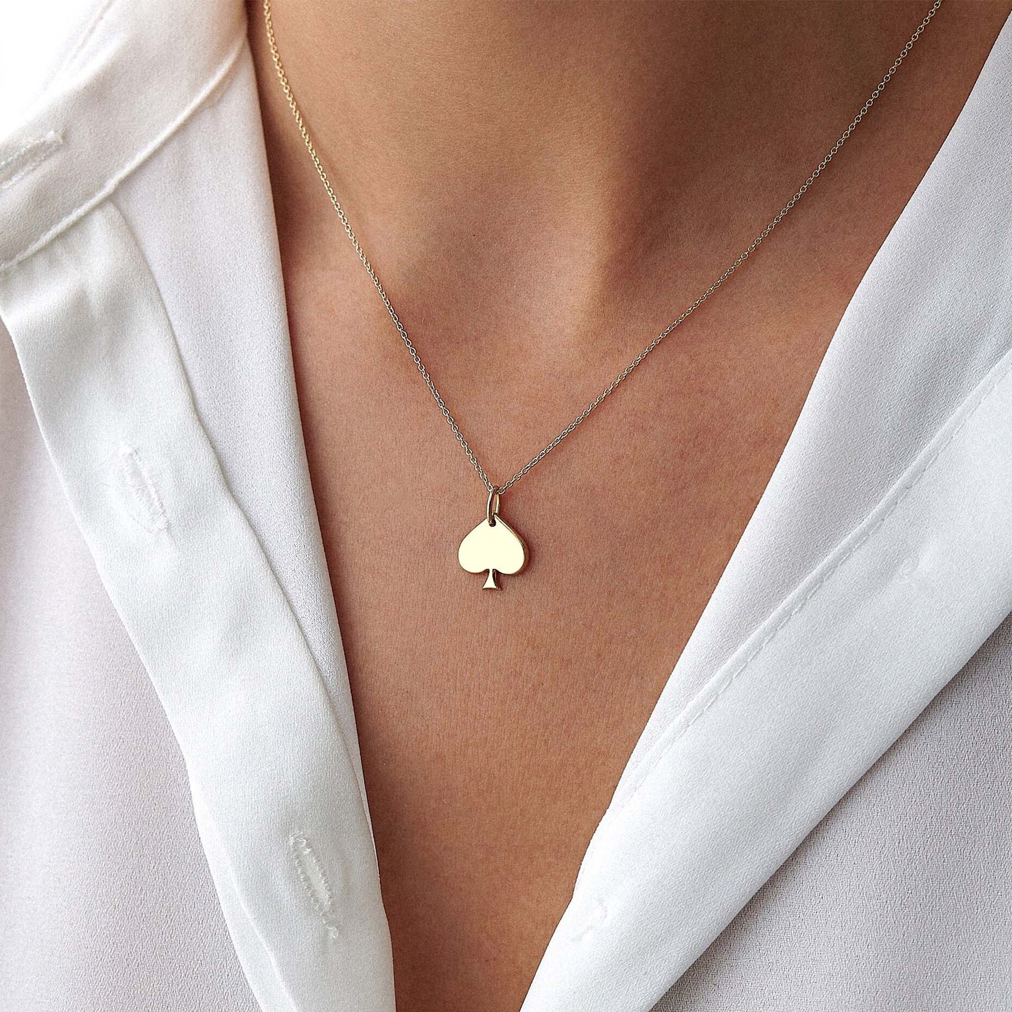 Gold necklace with a spade-shaped pendant worn by a person in a white shirt.