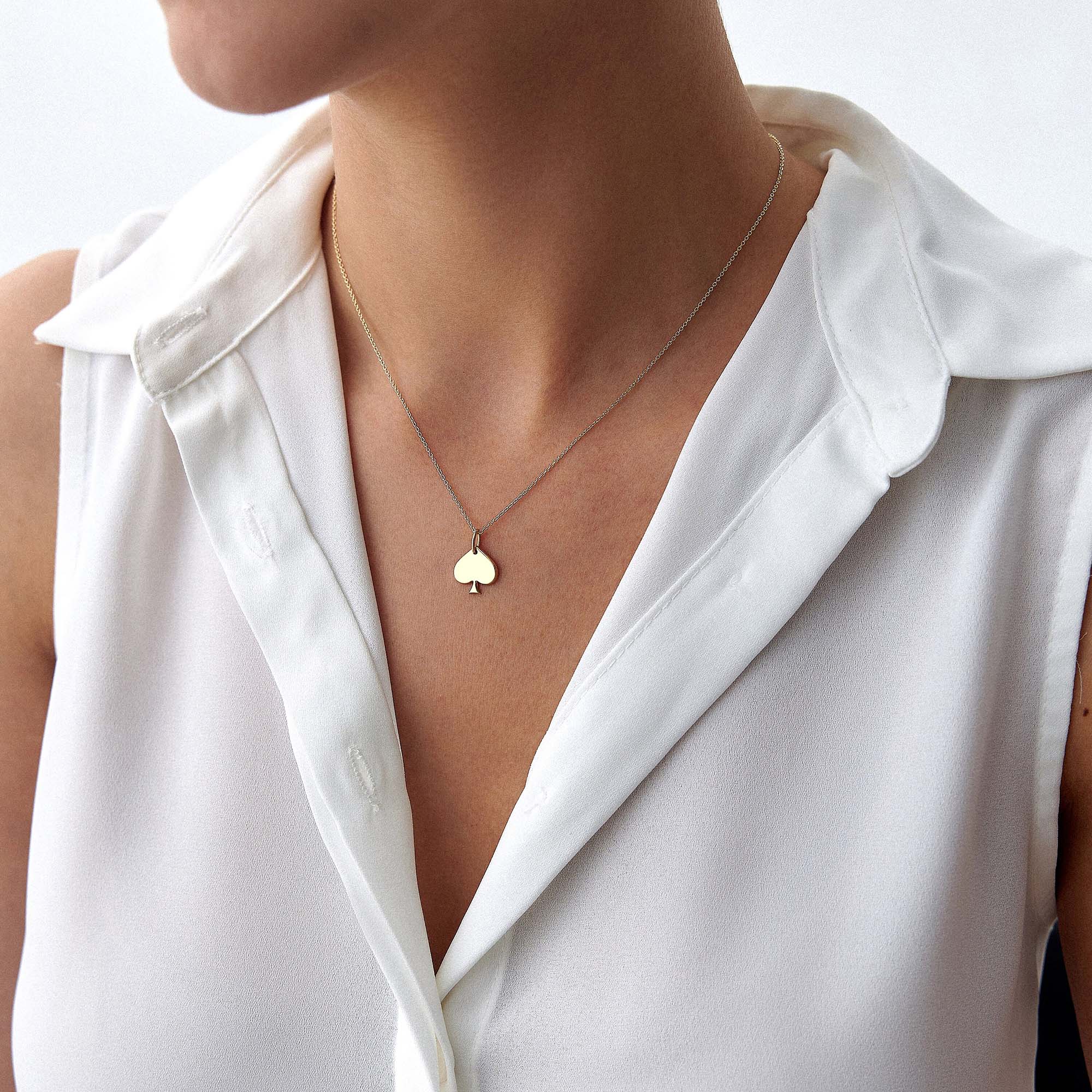 Gold necklace with a spade-shaped pendant worn by a person in a white shirt.