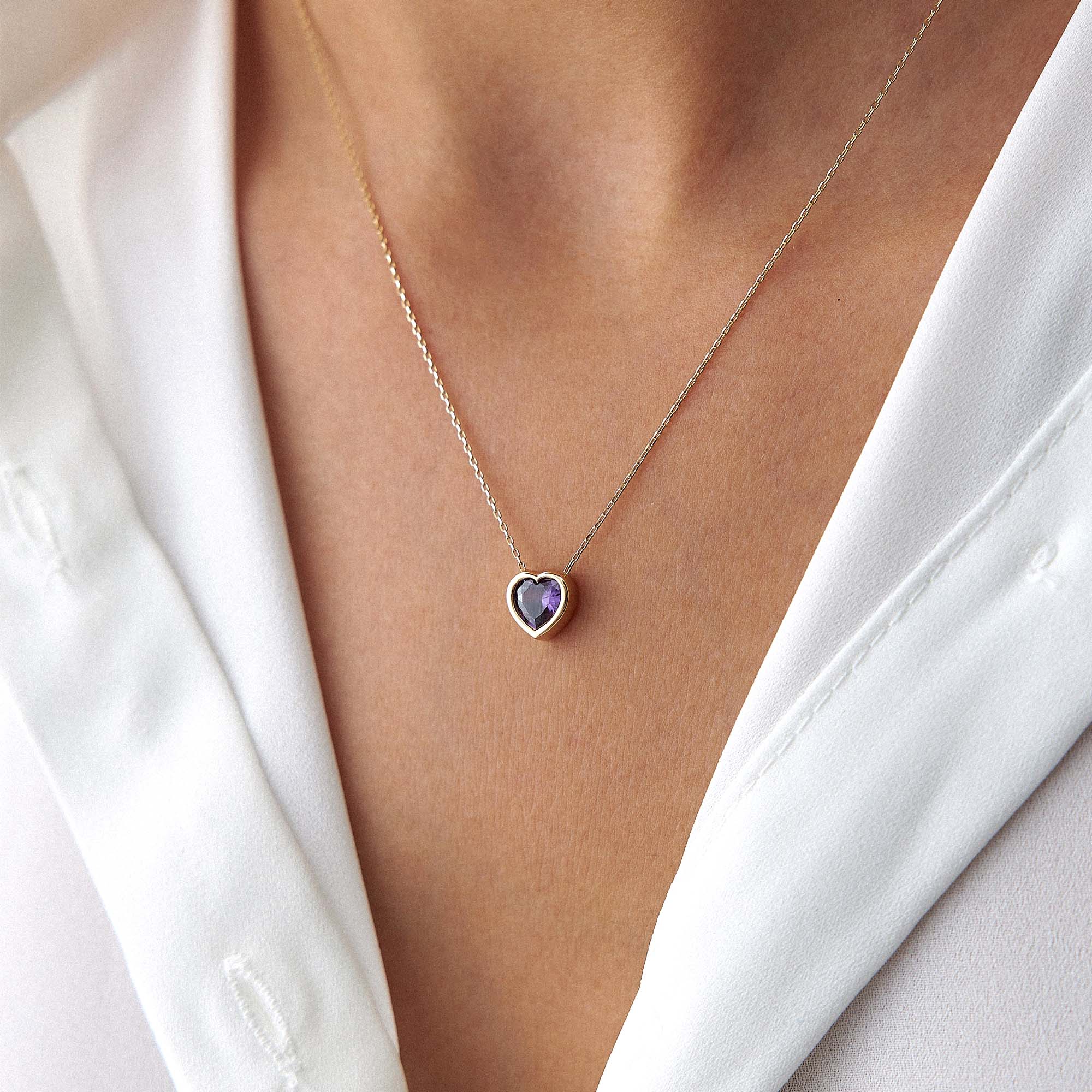 An upclose image of a model wearing a purple centered heart necklace