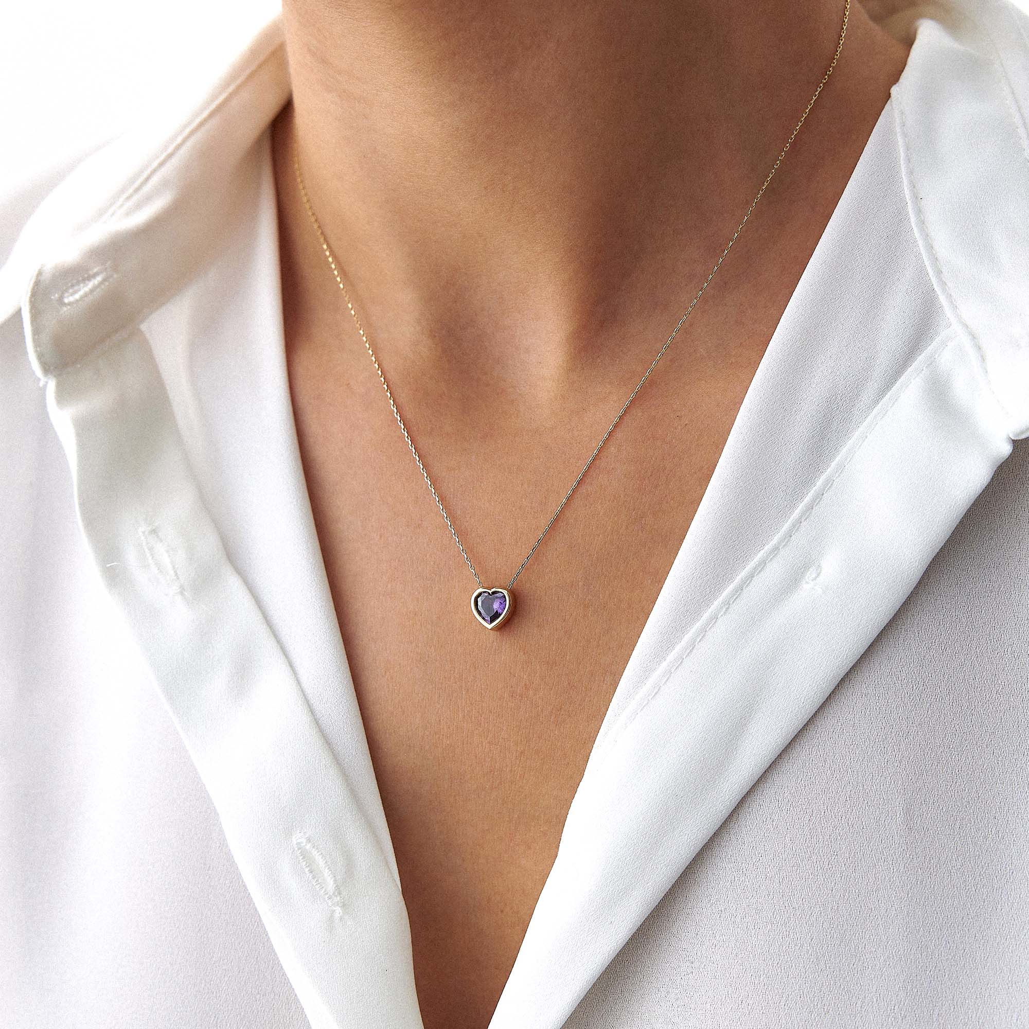 An upclose image of a model wearing a purple centered heart necklace