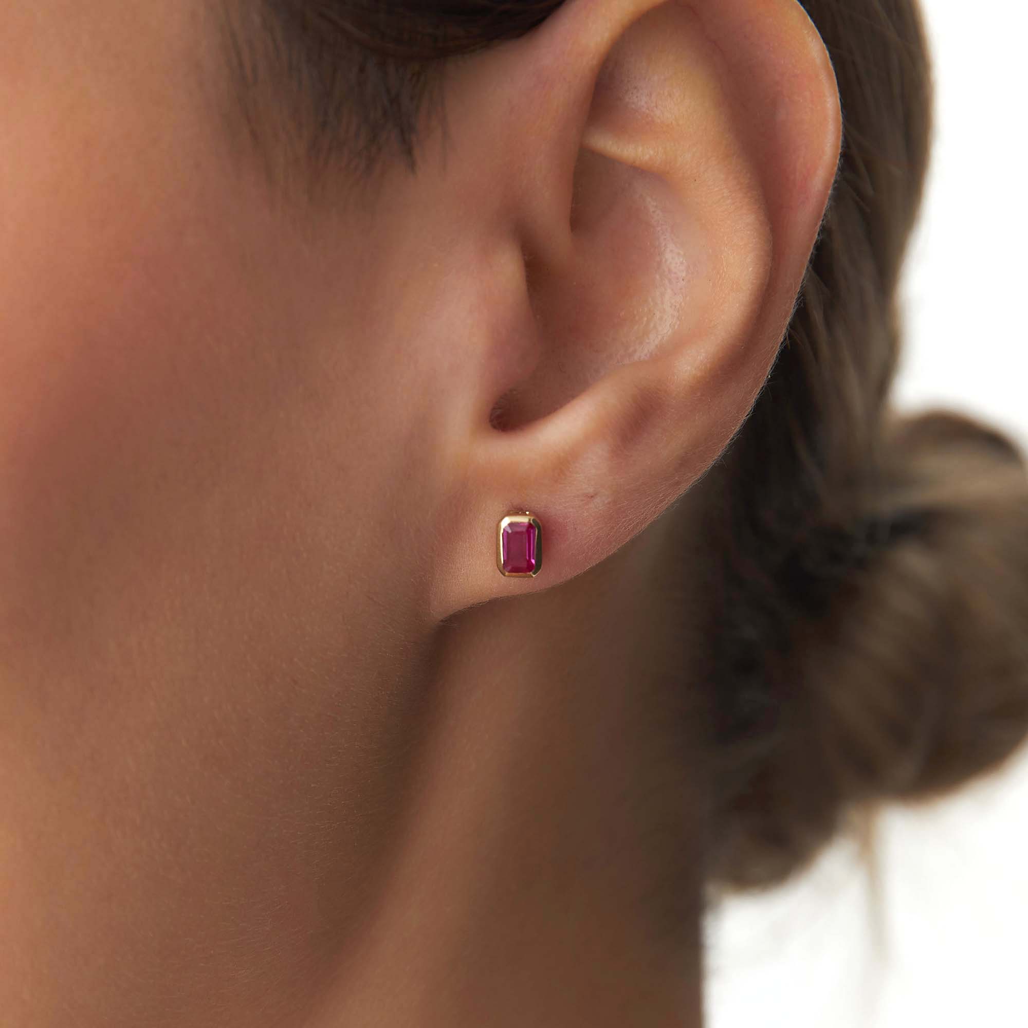 Close-up of an ear wearing a red gemstone earring with a blurred background