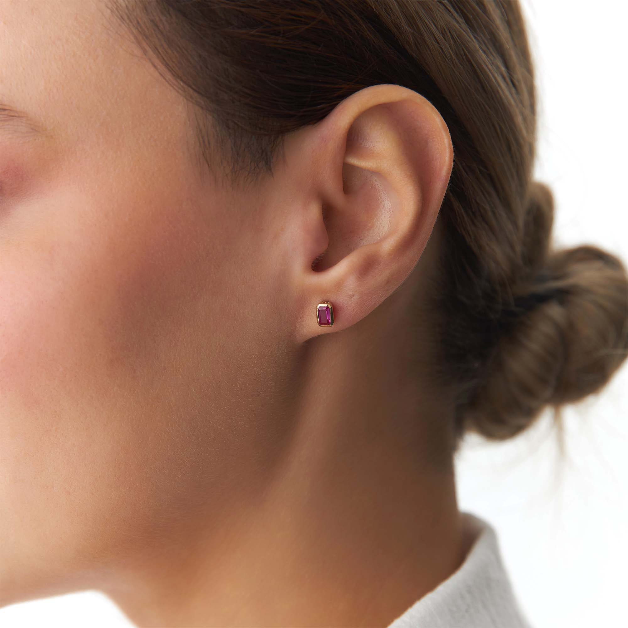 Close-up of an ear wearing a red gemstone earring with a blurred background