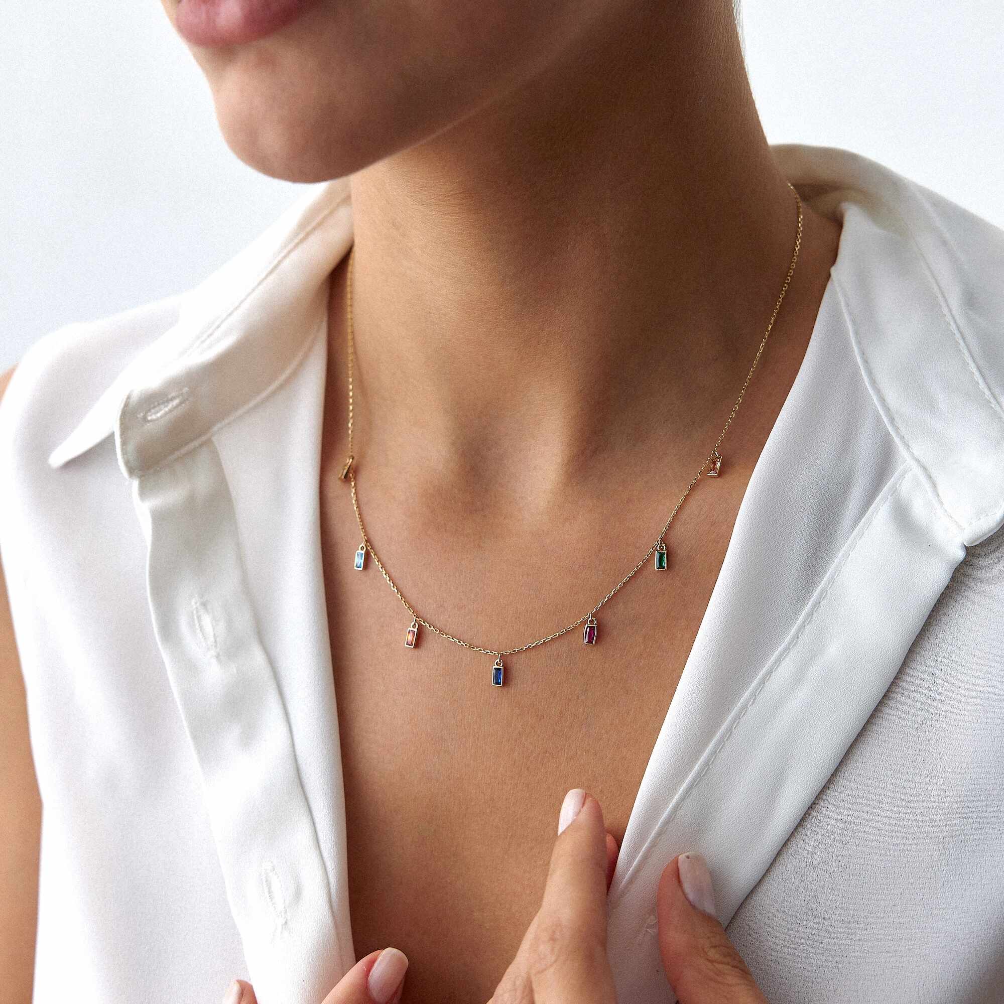 Necklace with small colorful charms worn by a person in a white shirt.