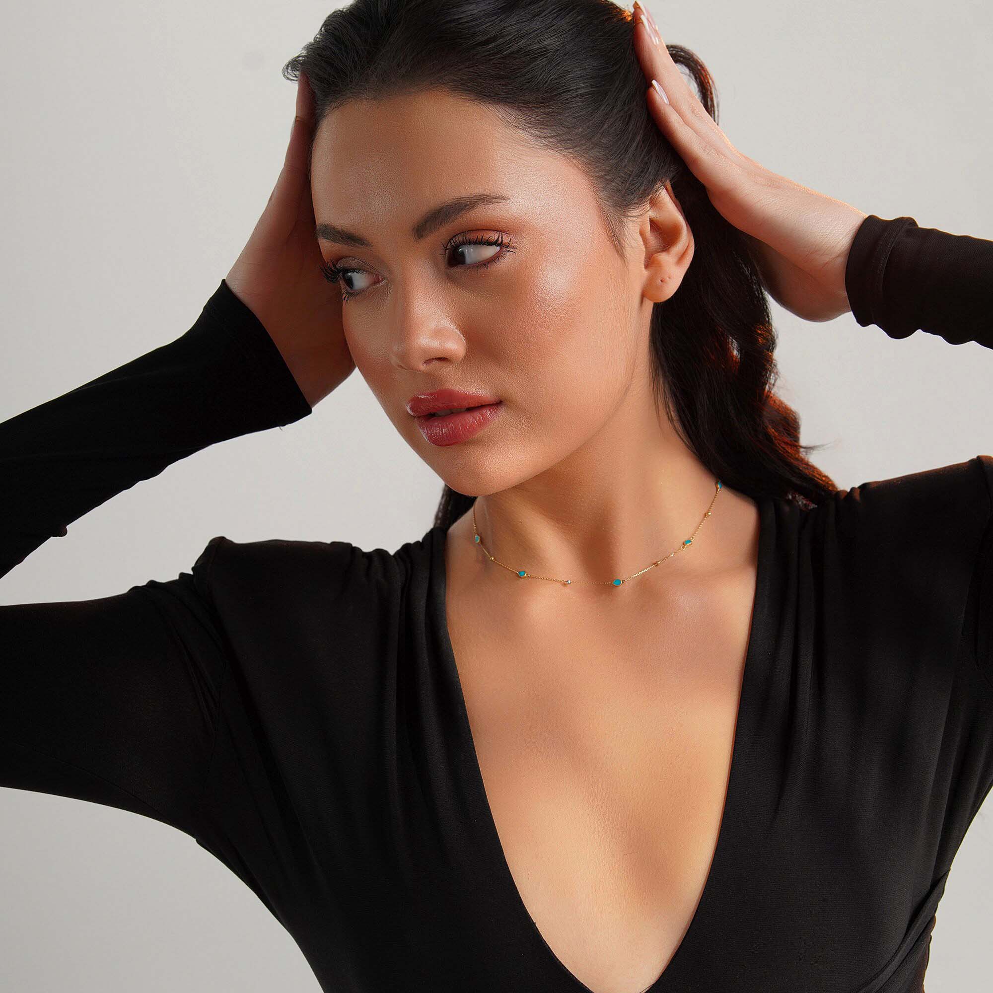 Woman wearing a raindrop station necklace against a neutral background