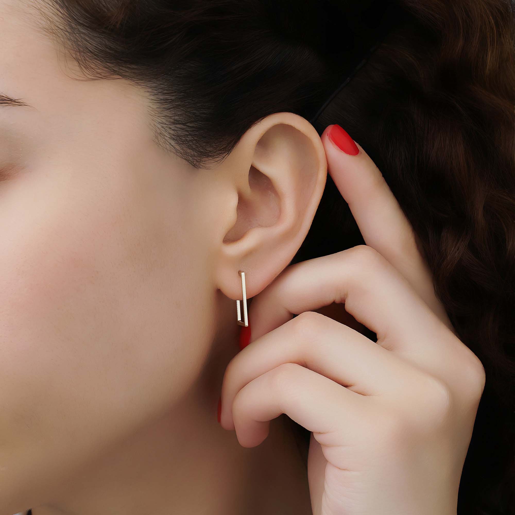 A close up of a model wearing a rectangle shaped 14k yellow gold stud earring.
