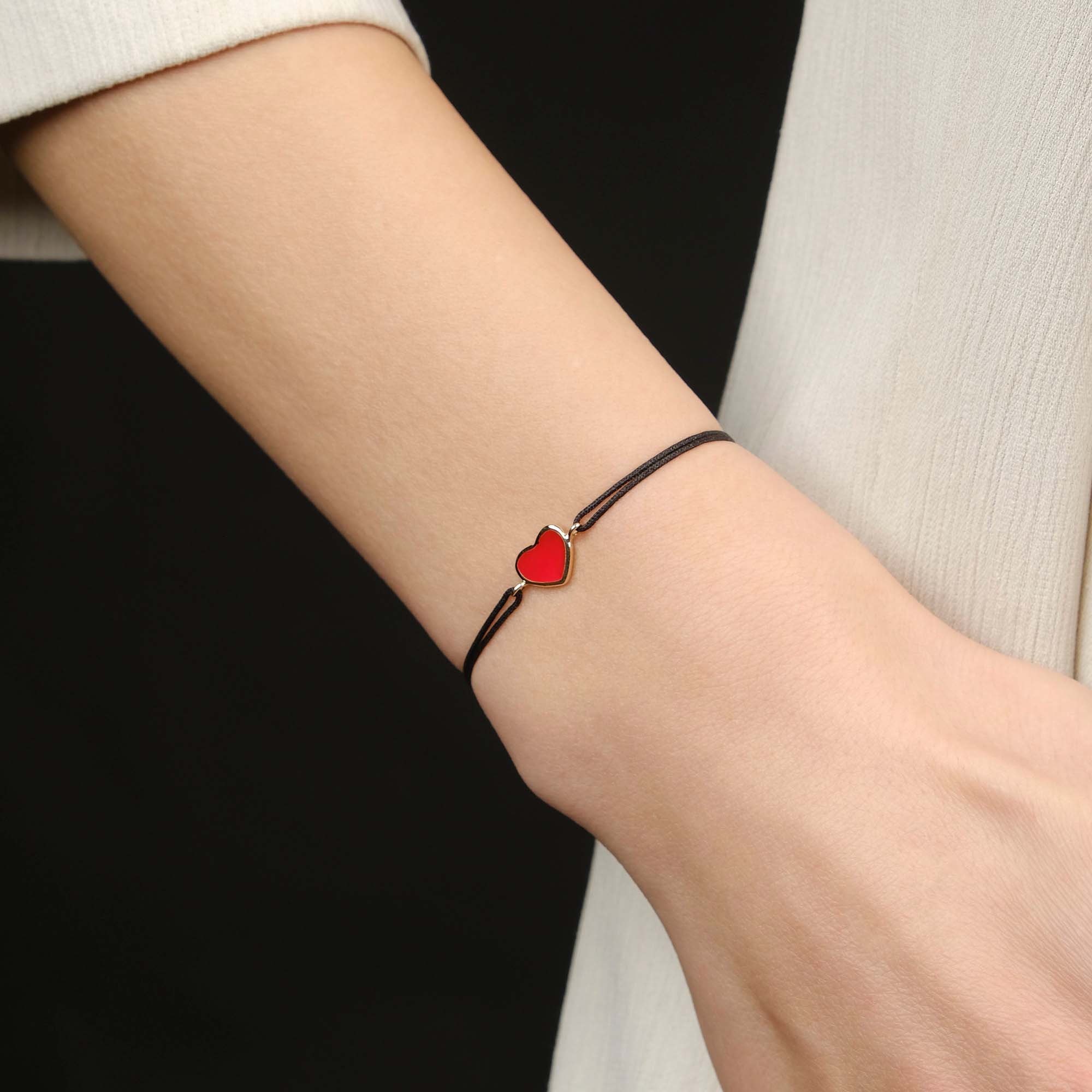 Bracelet with a red heart charm on a wrist against a black background