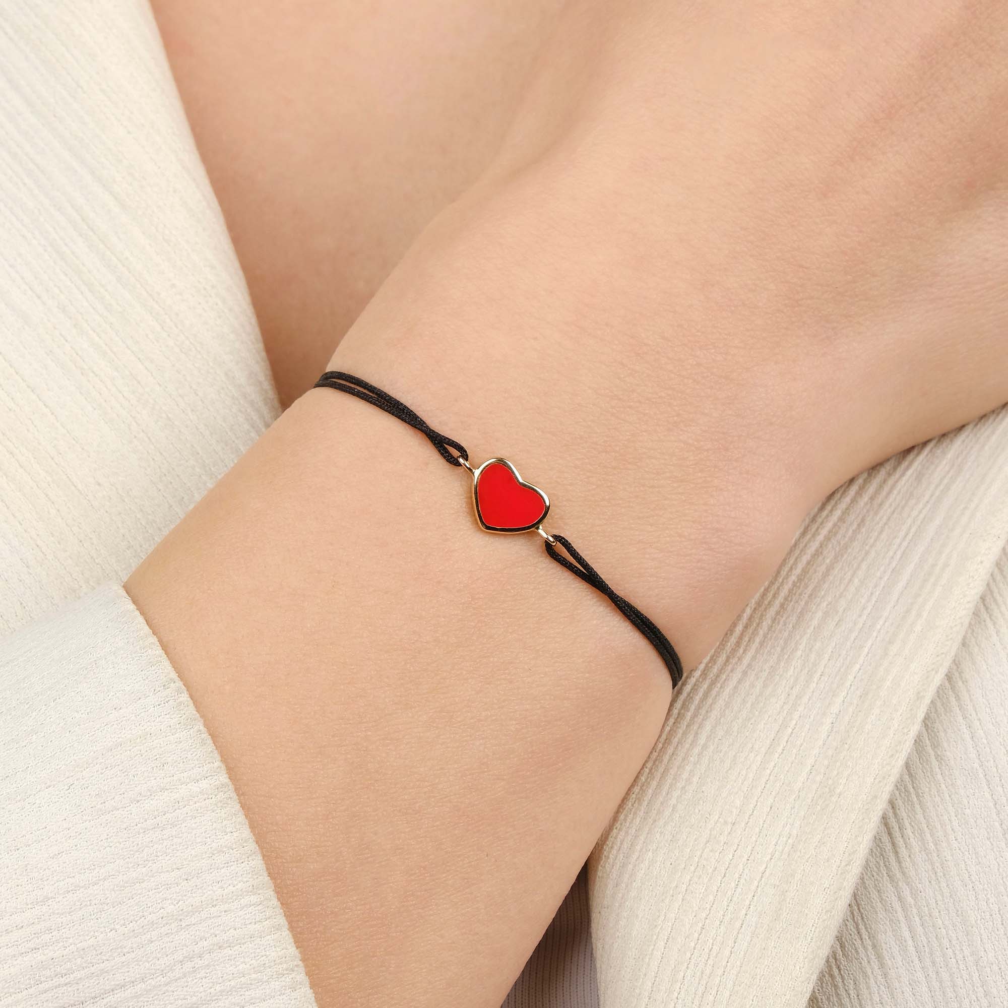 Bracelet with a red heart charm on a wrist against a neutral background