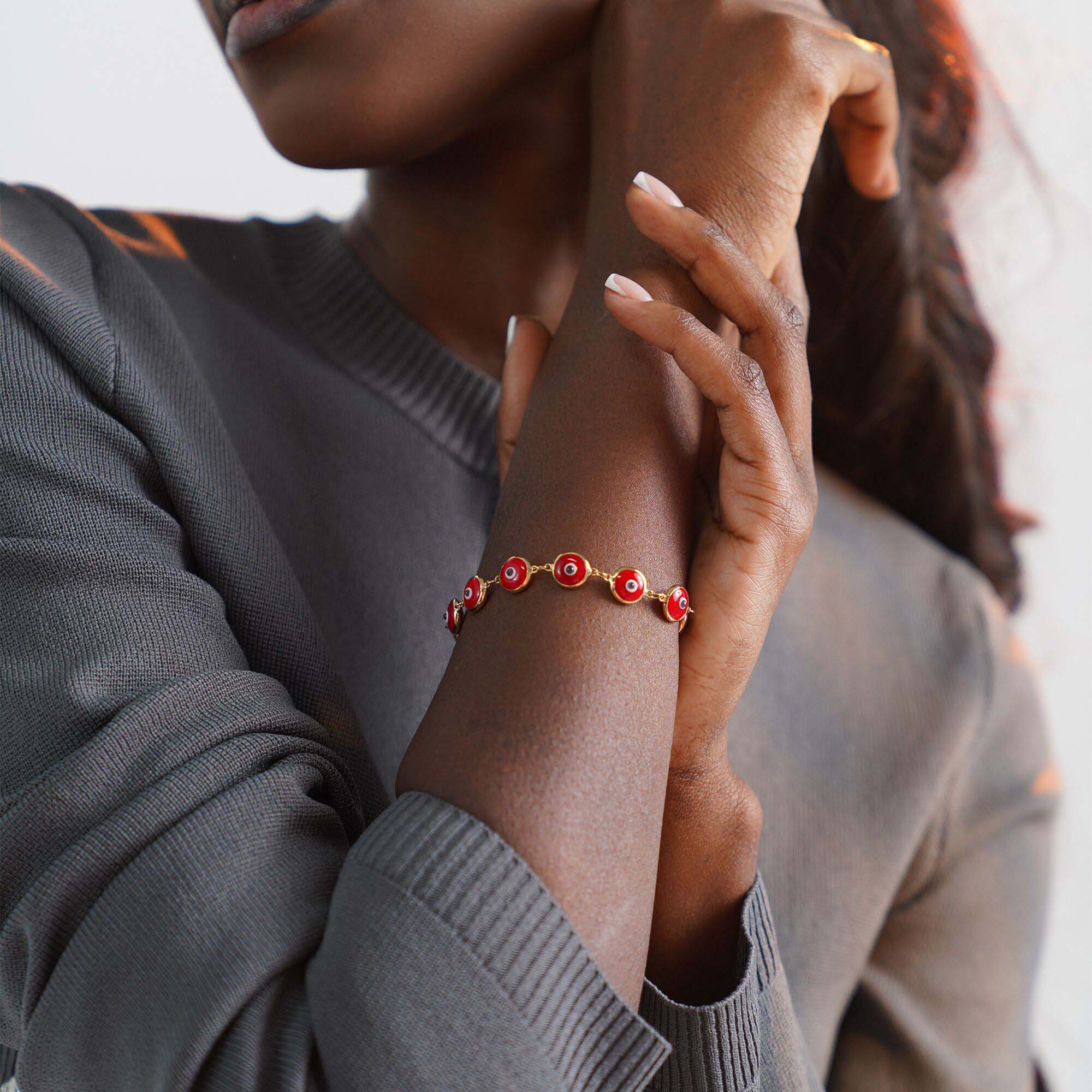 Person wearing a red evil eye bracelet on a blurred background